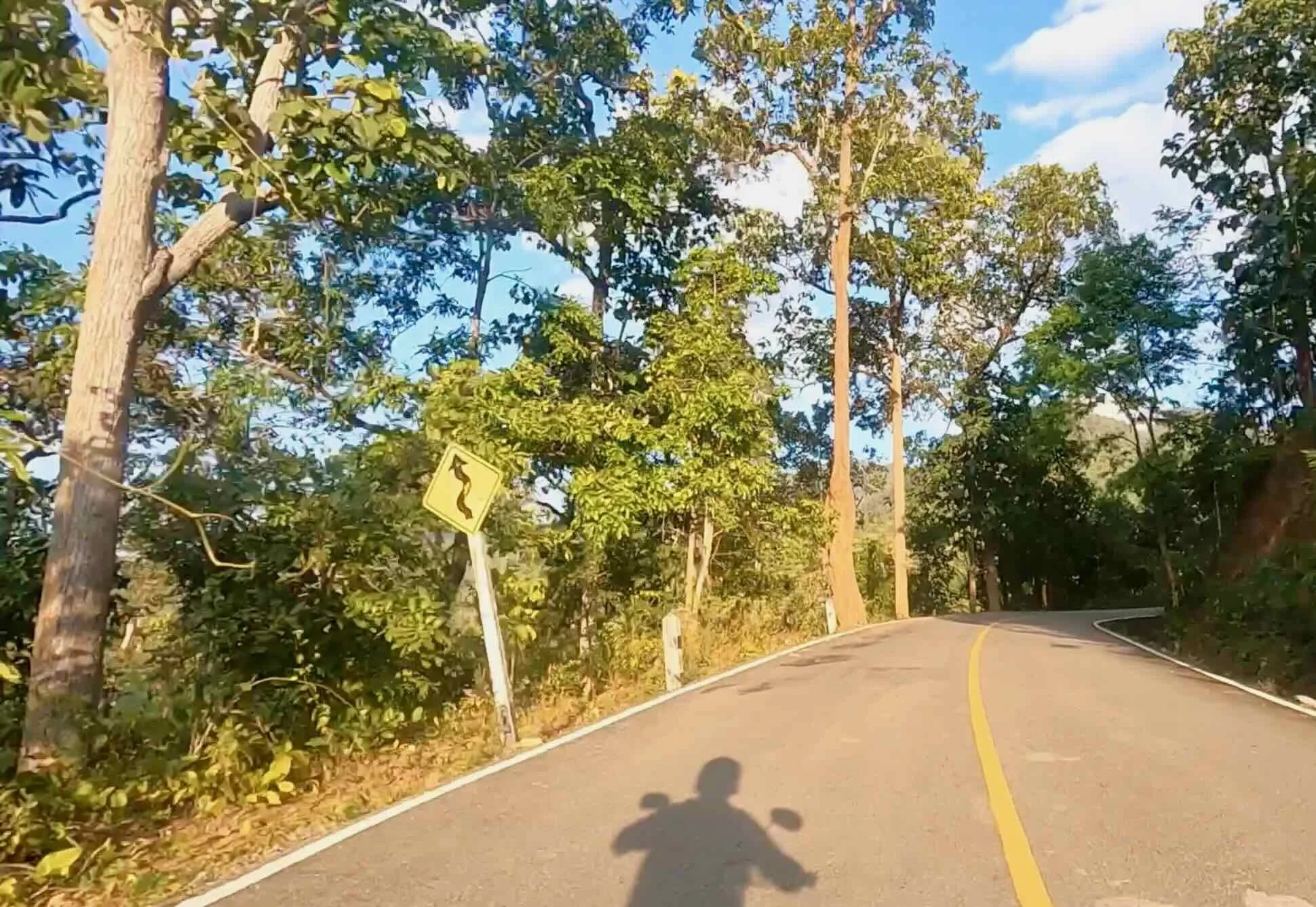 Road through the hills with shadow of the author riding on the road.