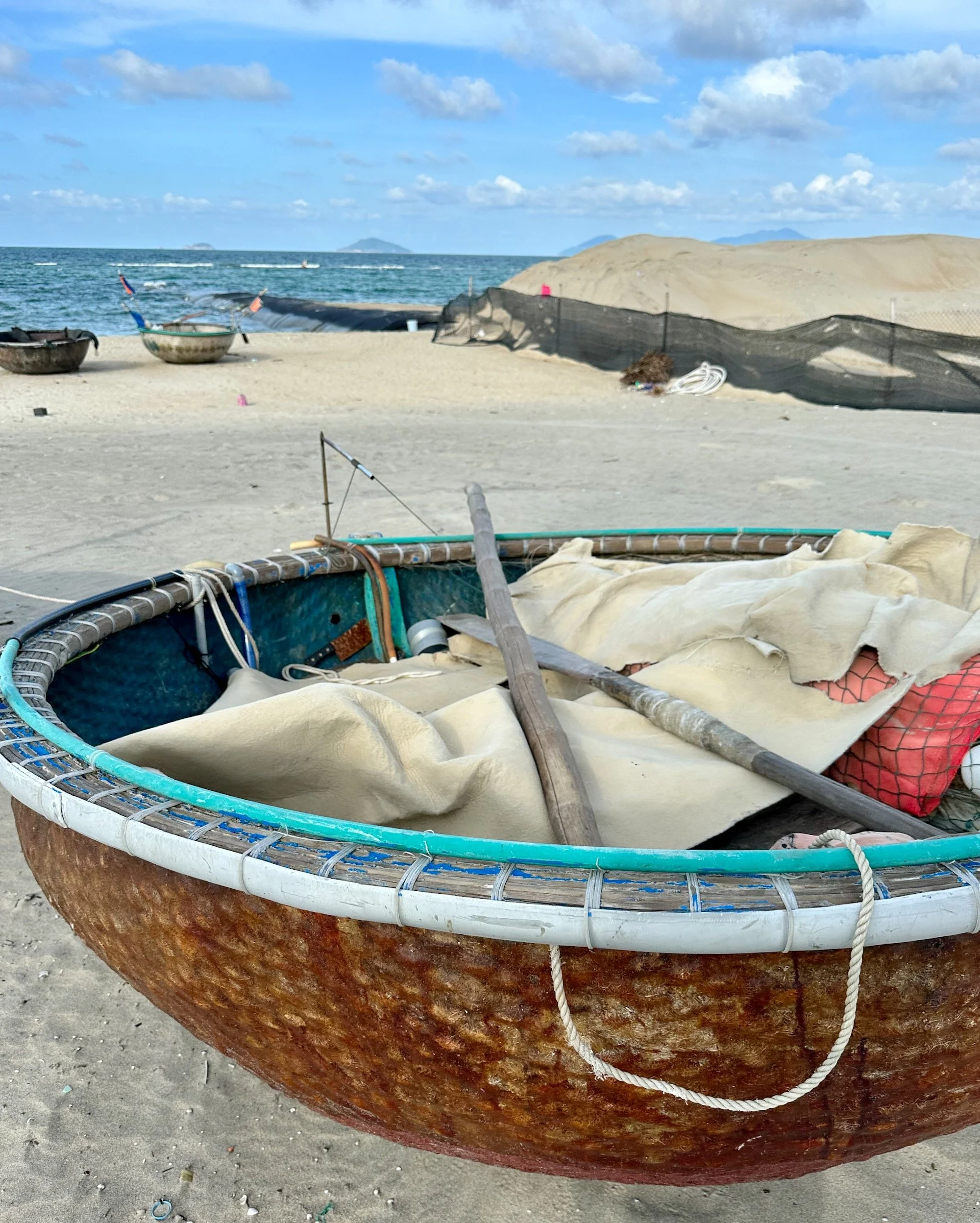 A basket boat on the beach in central Vietnam with oars and nets inside.