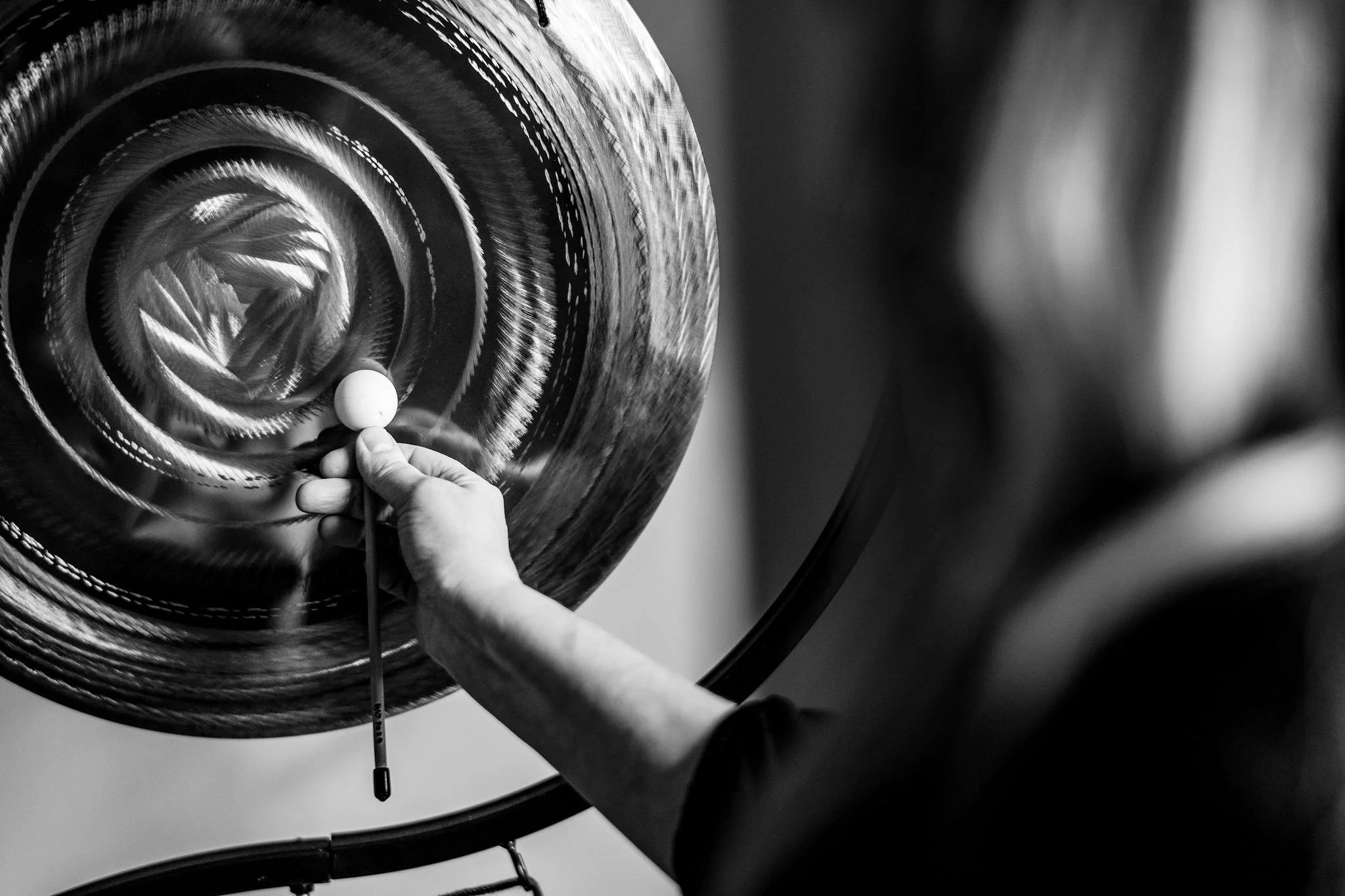 A person painting a large circular design with a small brush on a wall, in black and white