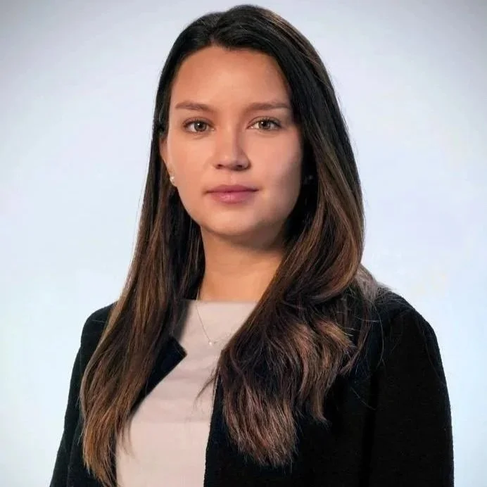 Professional headshot of a woman with long brown hair wearing a black blazer against a light background
