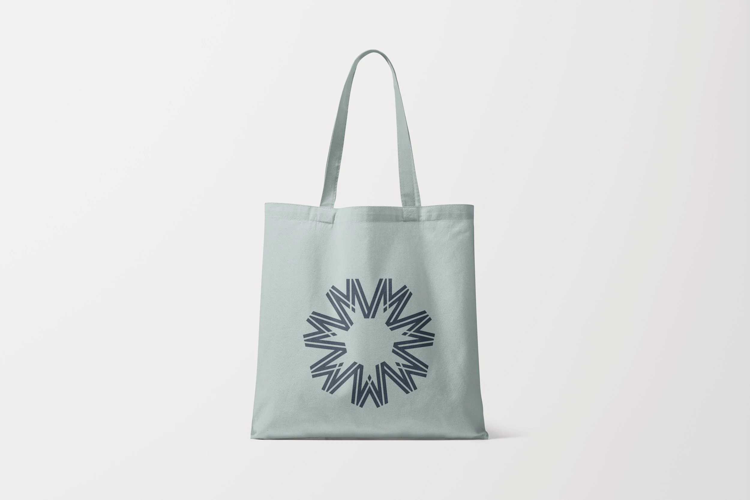Light gray tote bag with navy geometric starburst design on the front, set against a plain white background.