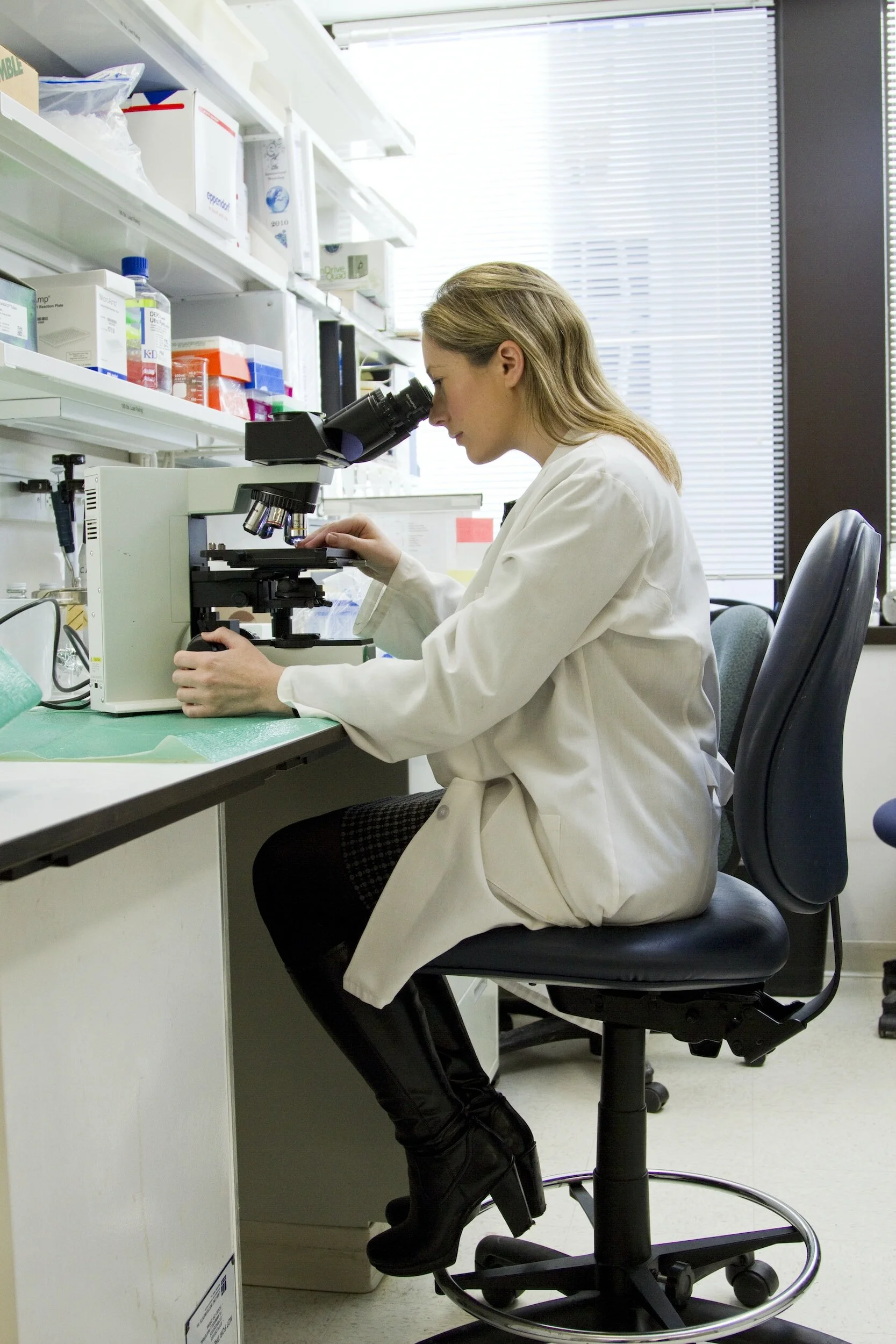 Woman in white coat using microscope in a lab