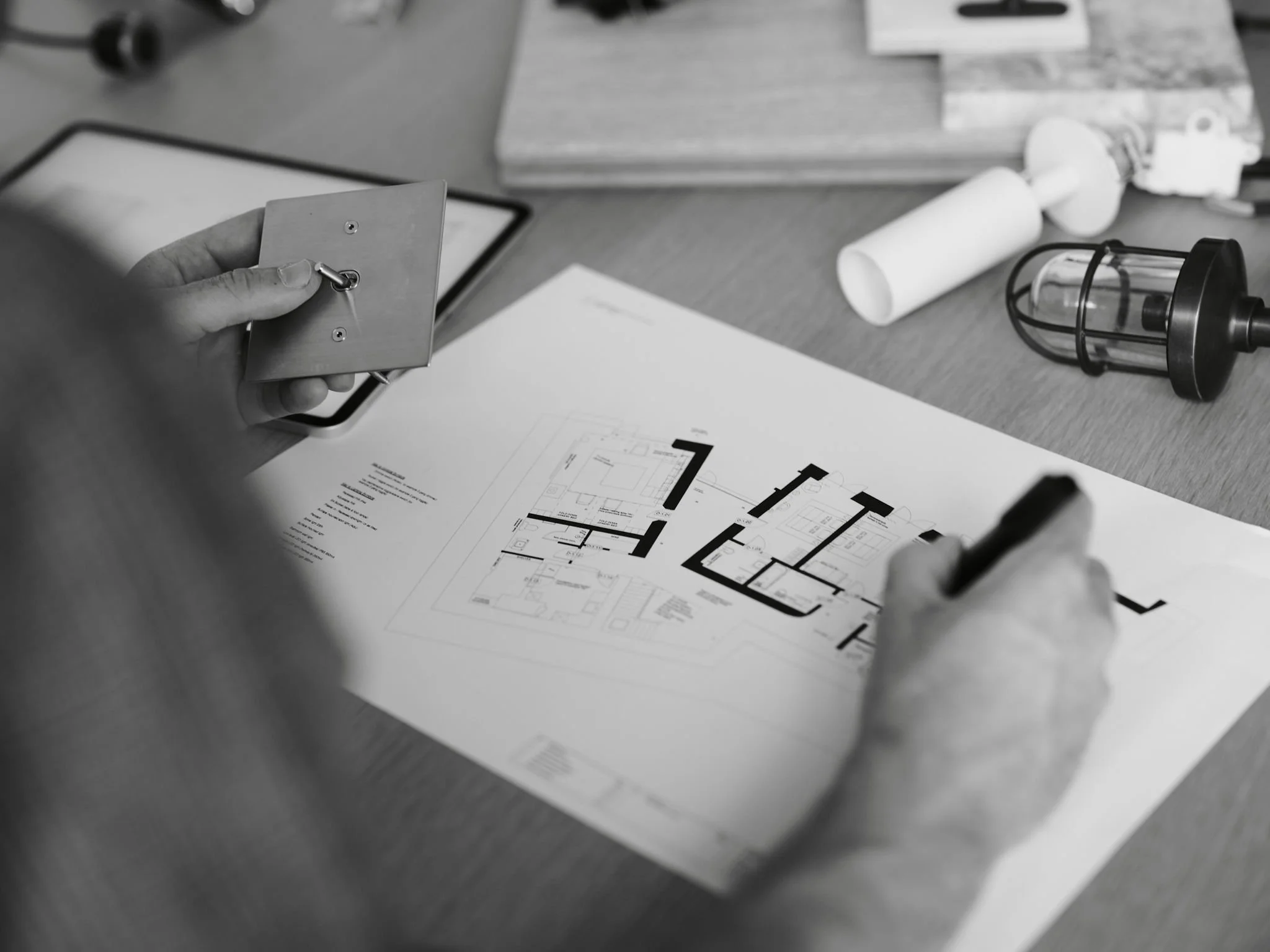 Interior Designer in Cornwall, Flo Millard and Lighting Designer in Cornwall, Chris Millard in their studio in Rock, North Cornwall. Person working on architectural plans with a pen, with various tools and a light fixture on the desk.