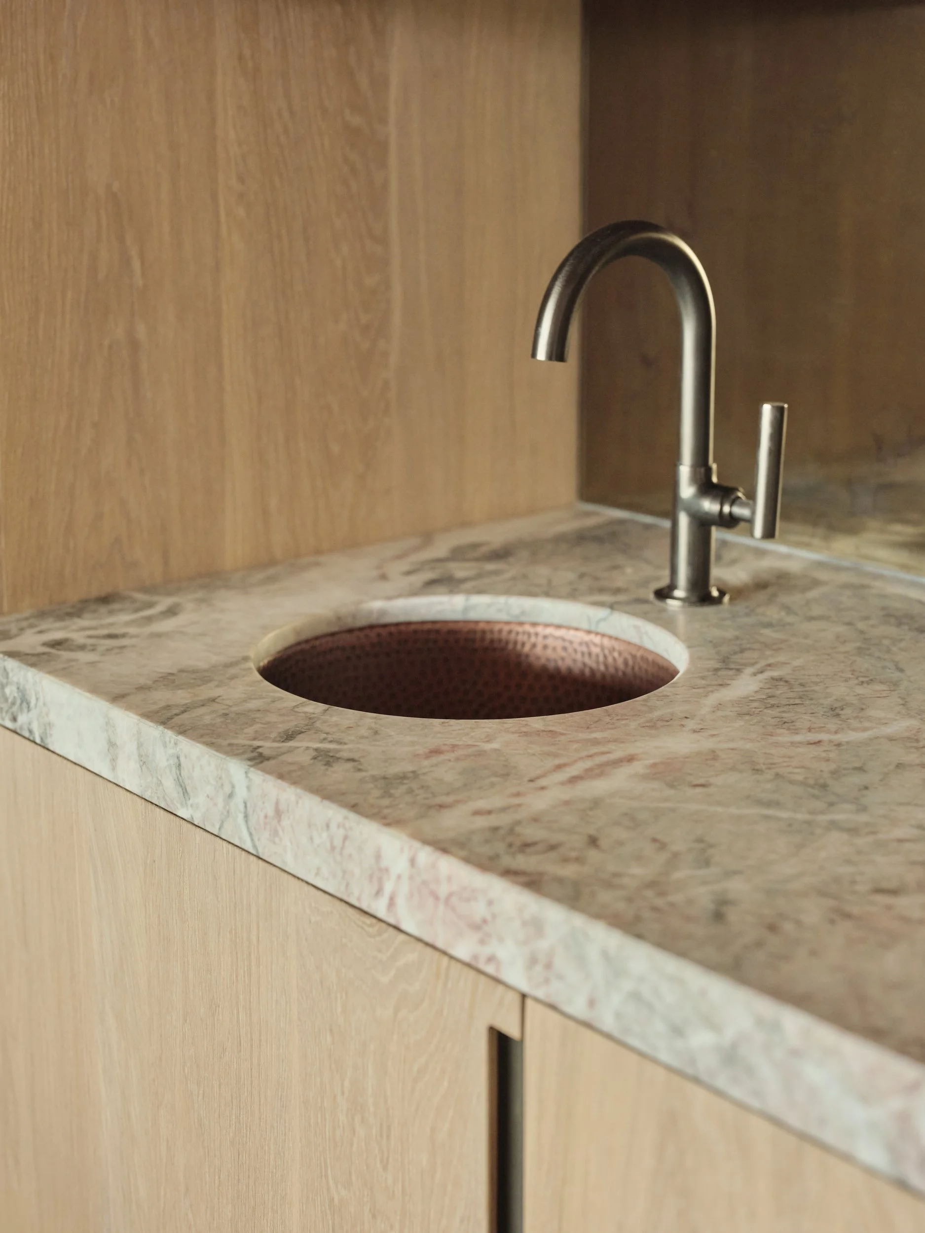 A kitchen sink with a marble countertop, a metallic faucet, and wooden cabinetry.