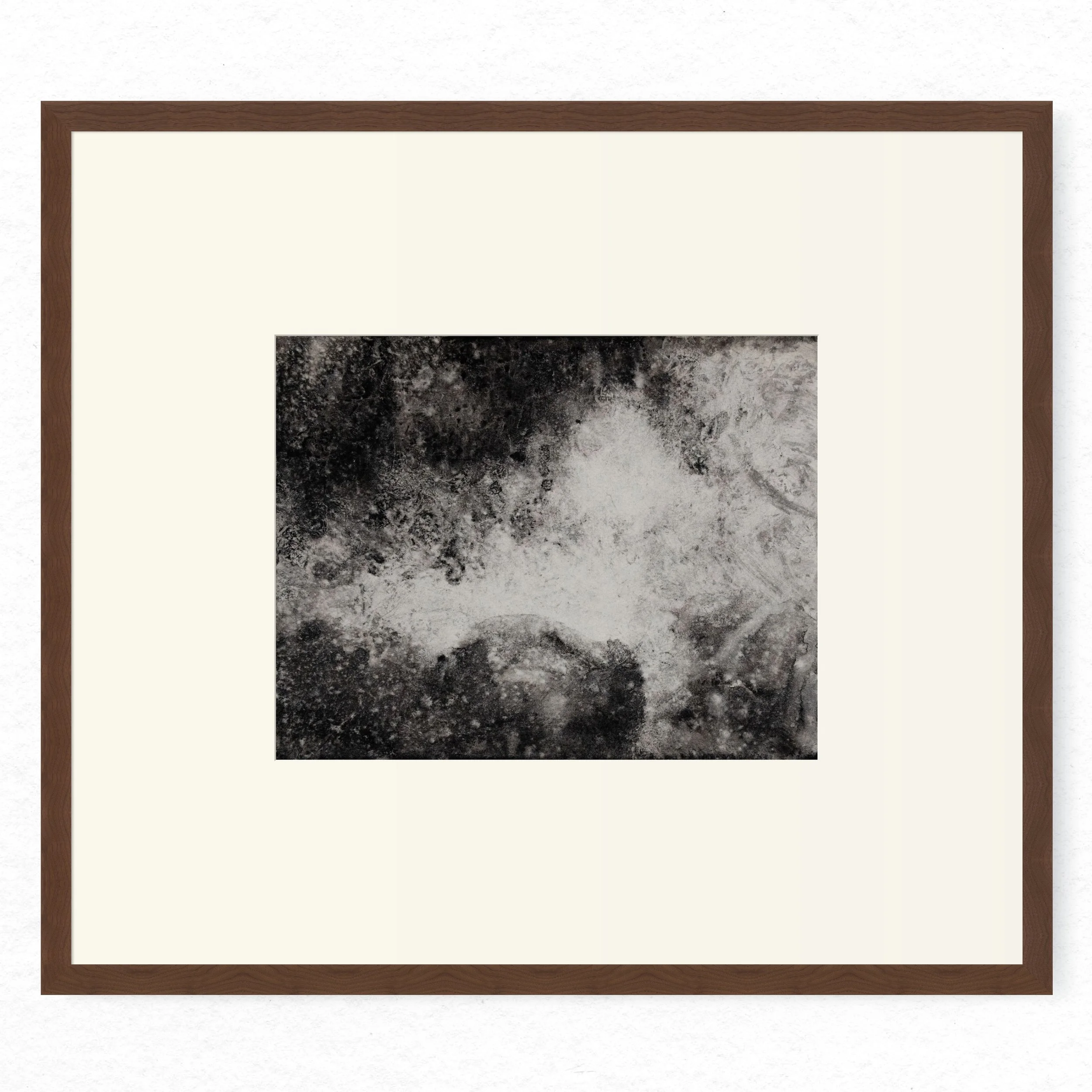 Shore 03 by Nicolas De Jesus — liquid charcoal and water on paper, waves crashing against rocks rendered in granular dark texture surrounding a bright central burst of spray, hardwood frame with mount
