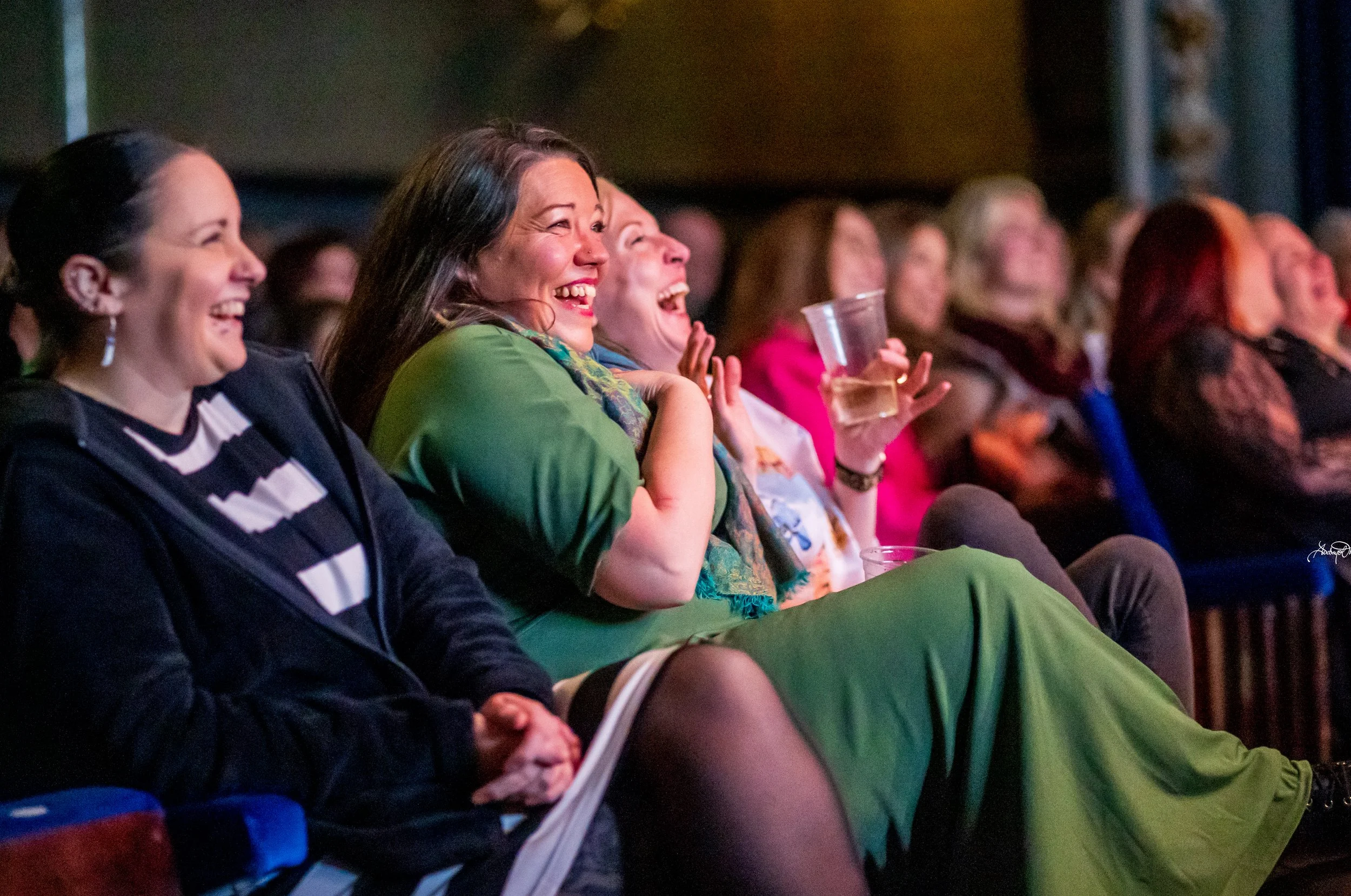 A group of women sitting together in an auditorium, laughing and enjoying a performance.