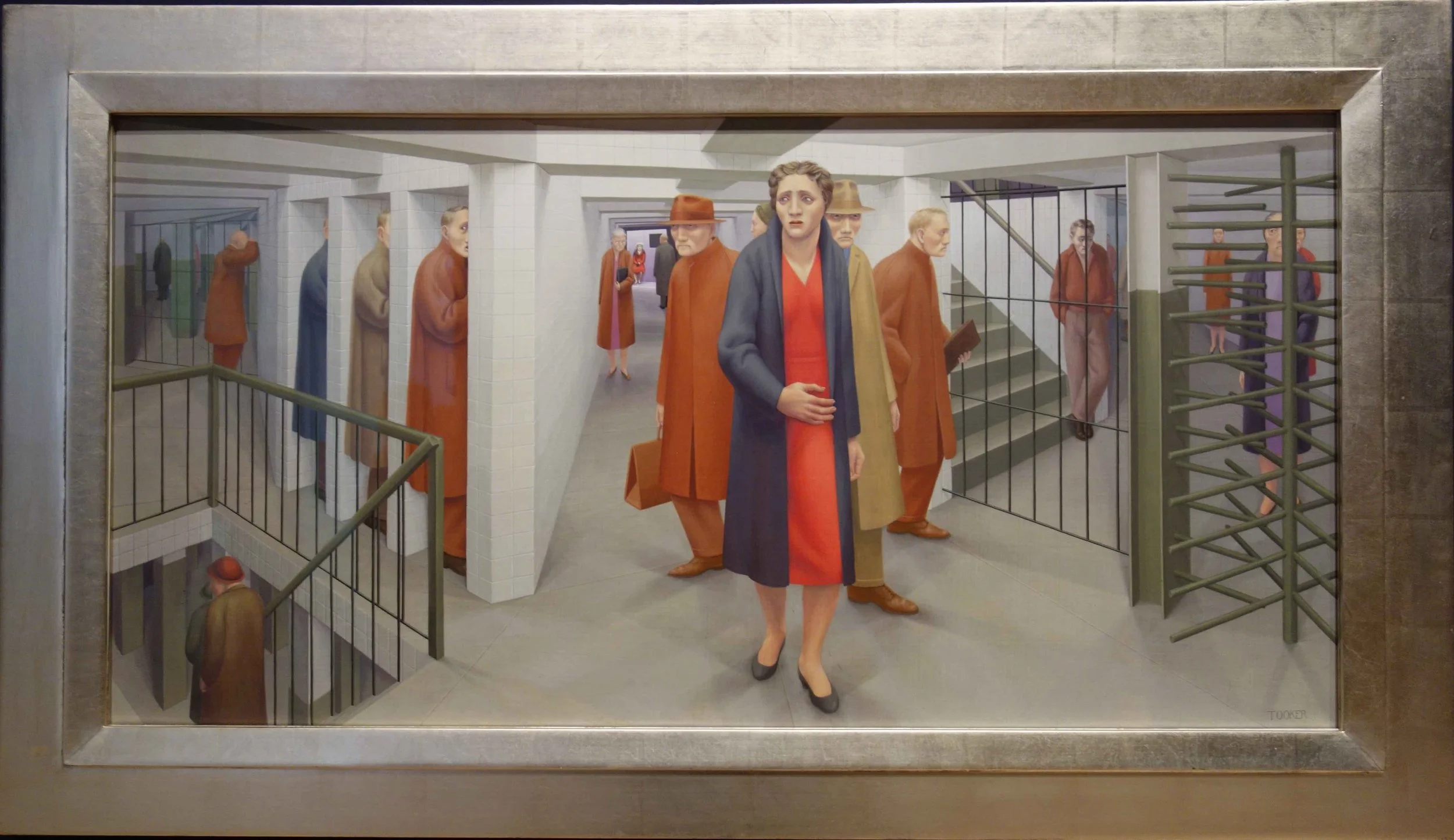 Una scena di un museo con sculture raffiguranti persone in attesa dietro sbarre, con molte persone della seconda guerra mondiale e uniformi. Al centro, una donna con un abito rosso e un cappotto blu sbracciato, davanti a tutte.