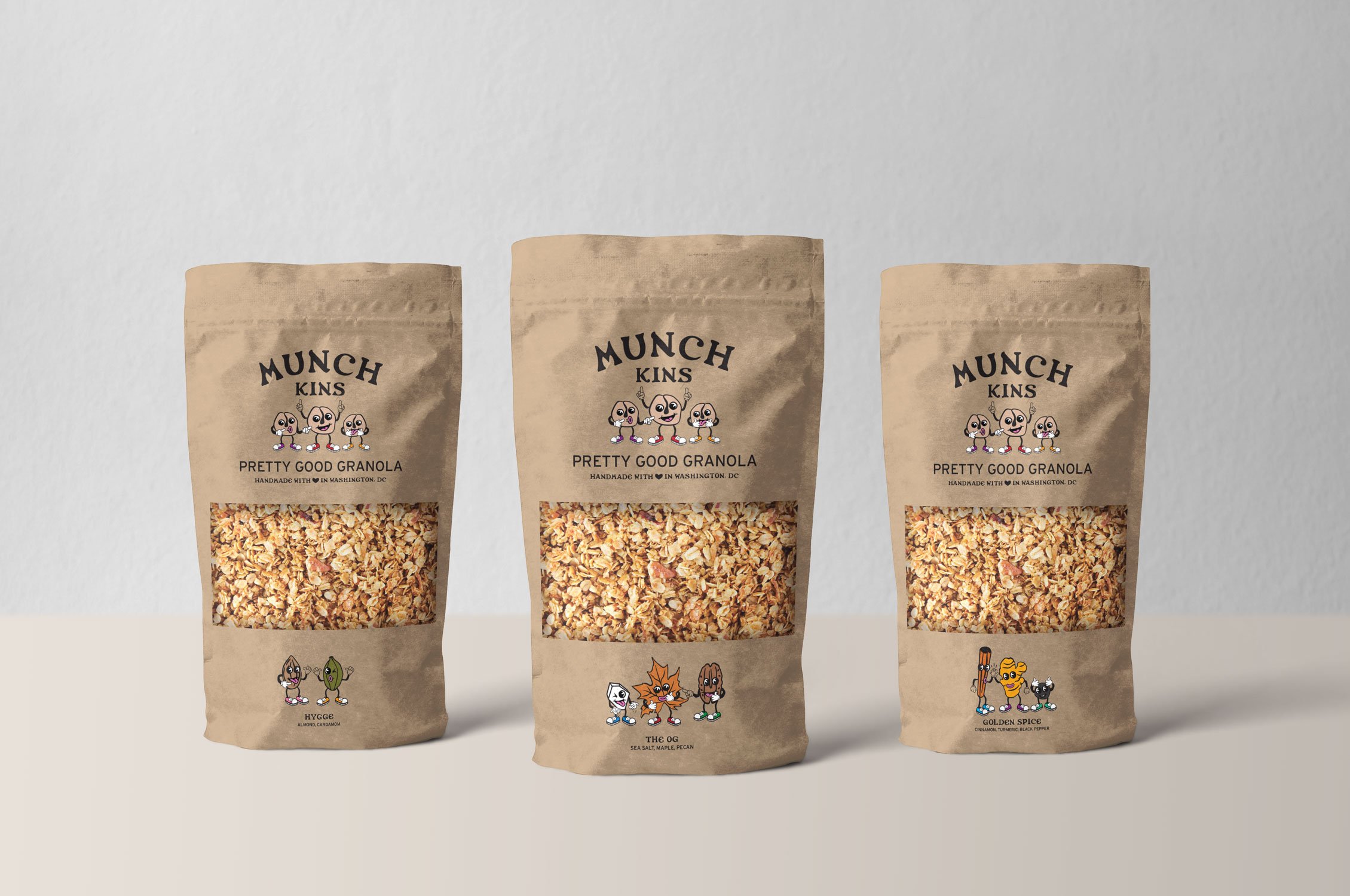 Three brown paper bags of Munch Kins Pretty Good Granola with cartoon characters on the bags, placed on a plain light background.
