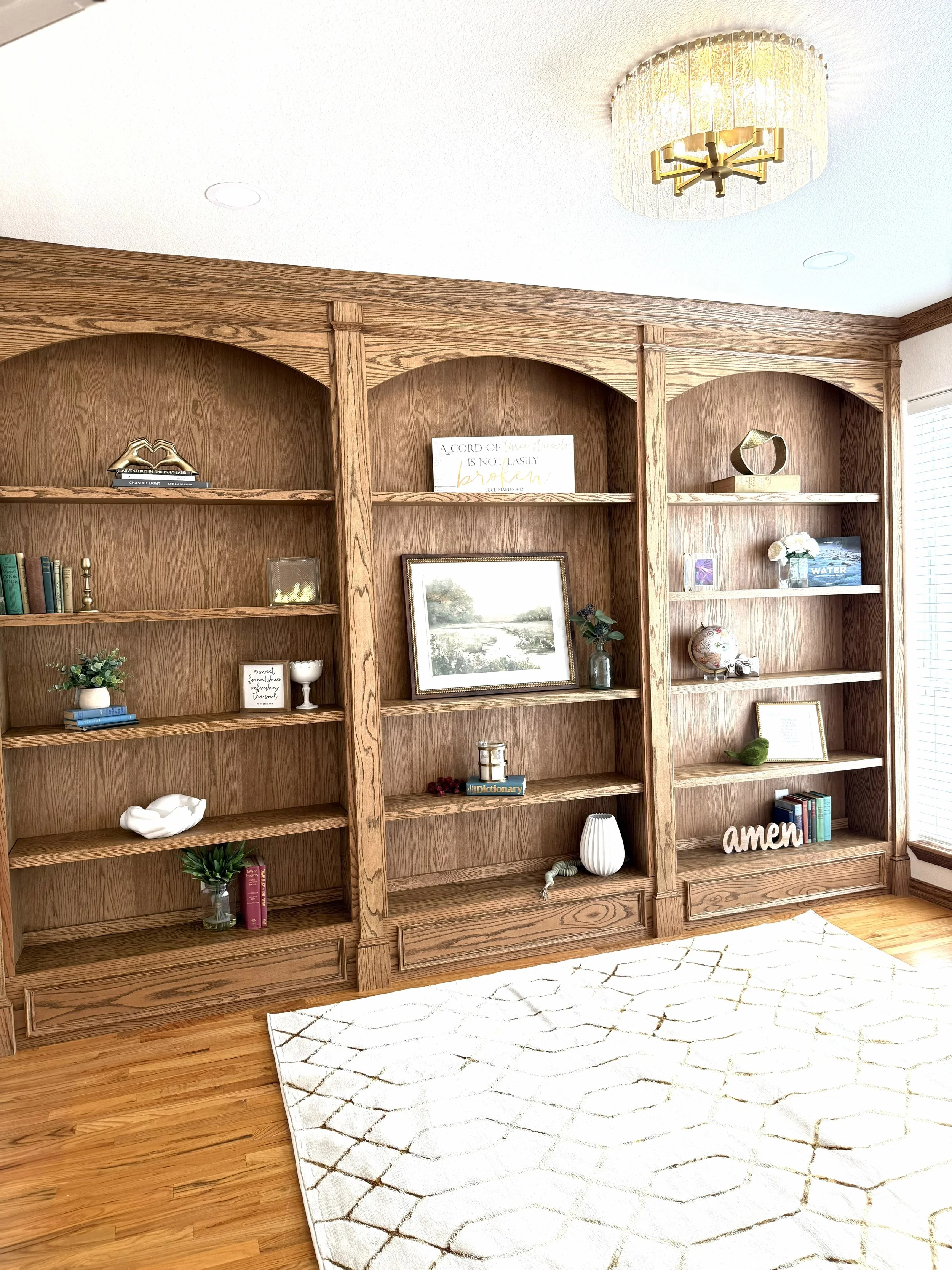 Custom built in shelves in a home office designed by an interior designer, showcasing arched wood book shelves with modern lighting
