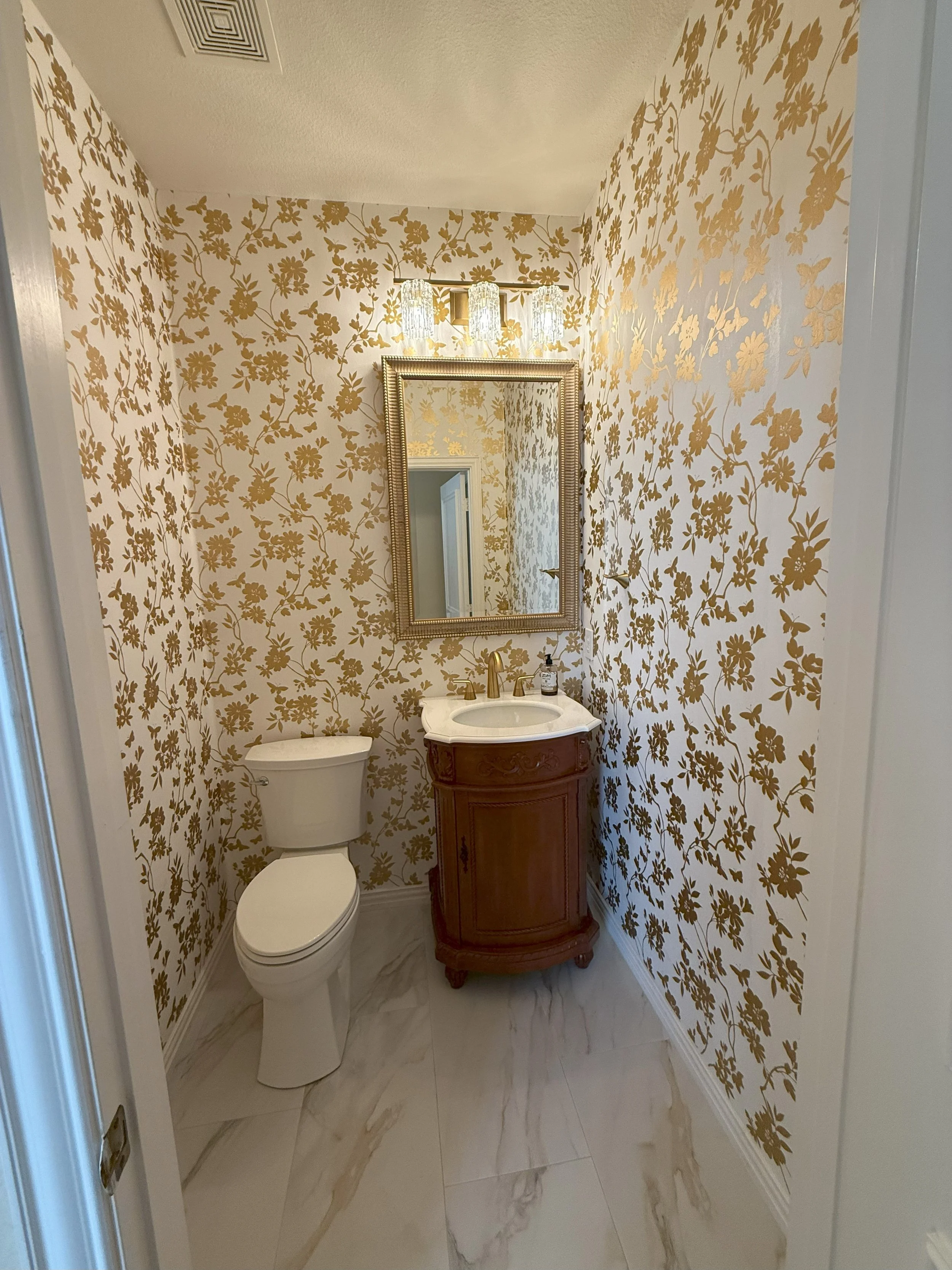 Luxury powder bathroom featuring gold botanical wallpaper, classic wood vanity by Interior Designer in Flower Mound.