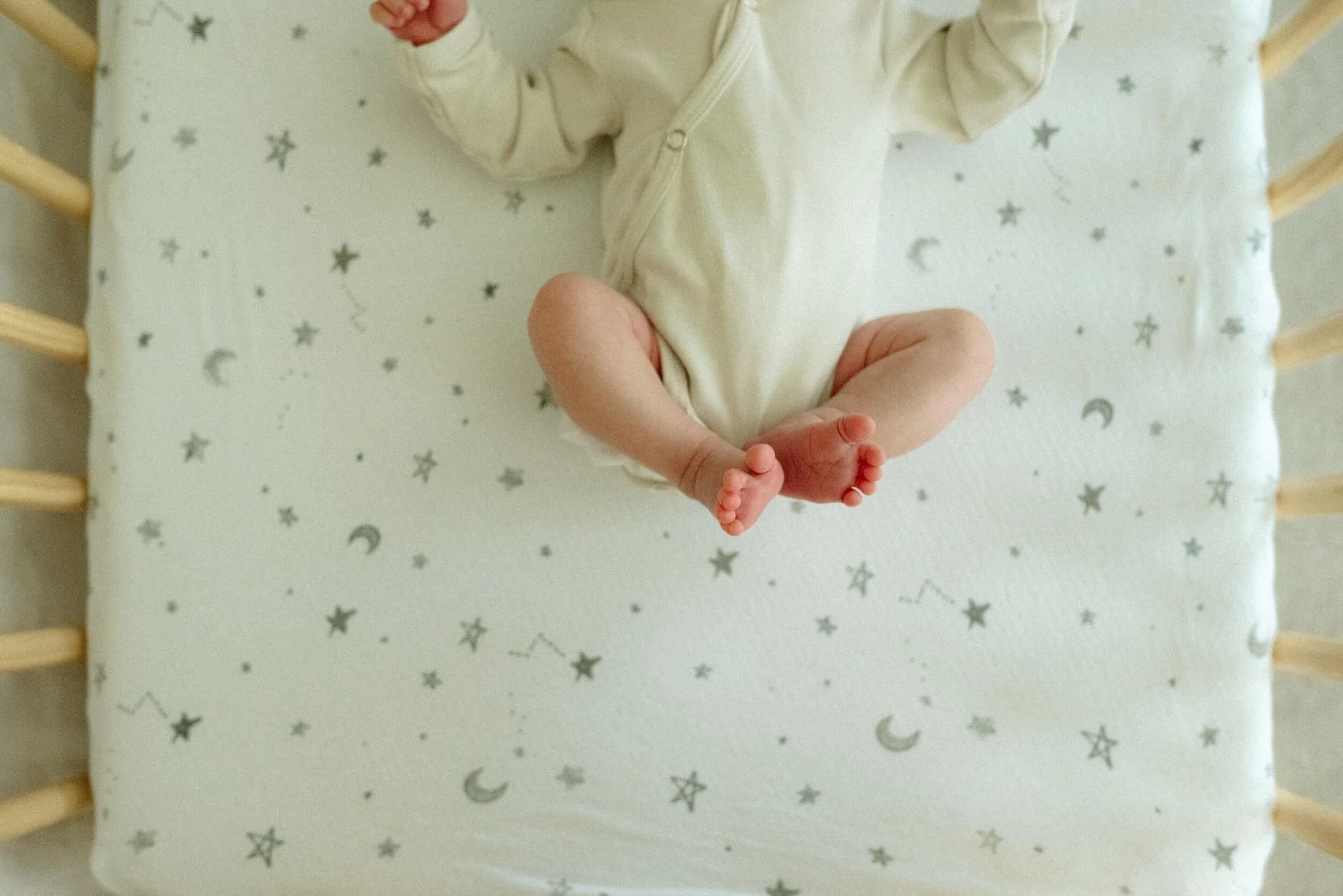a newborn resting peacefully in a crib with starry themed bedding, their tiny feet being documented beautifully by a New Braunfels newborn photographer, known for creating timeless keepsakes for families in New Braunfels, Tx.