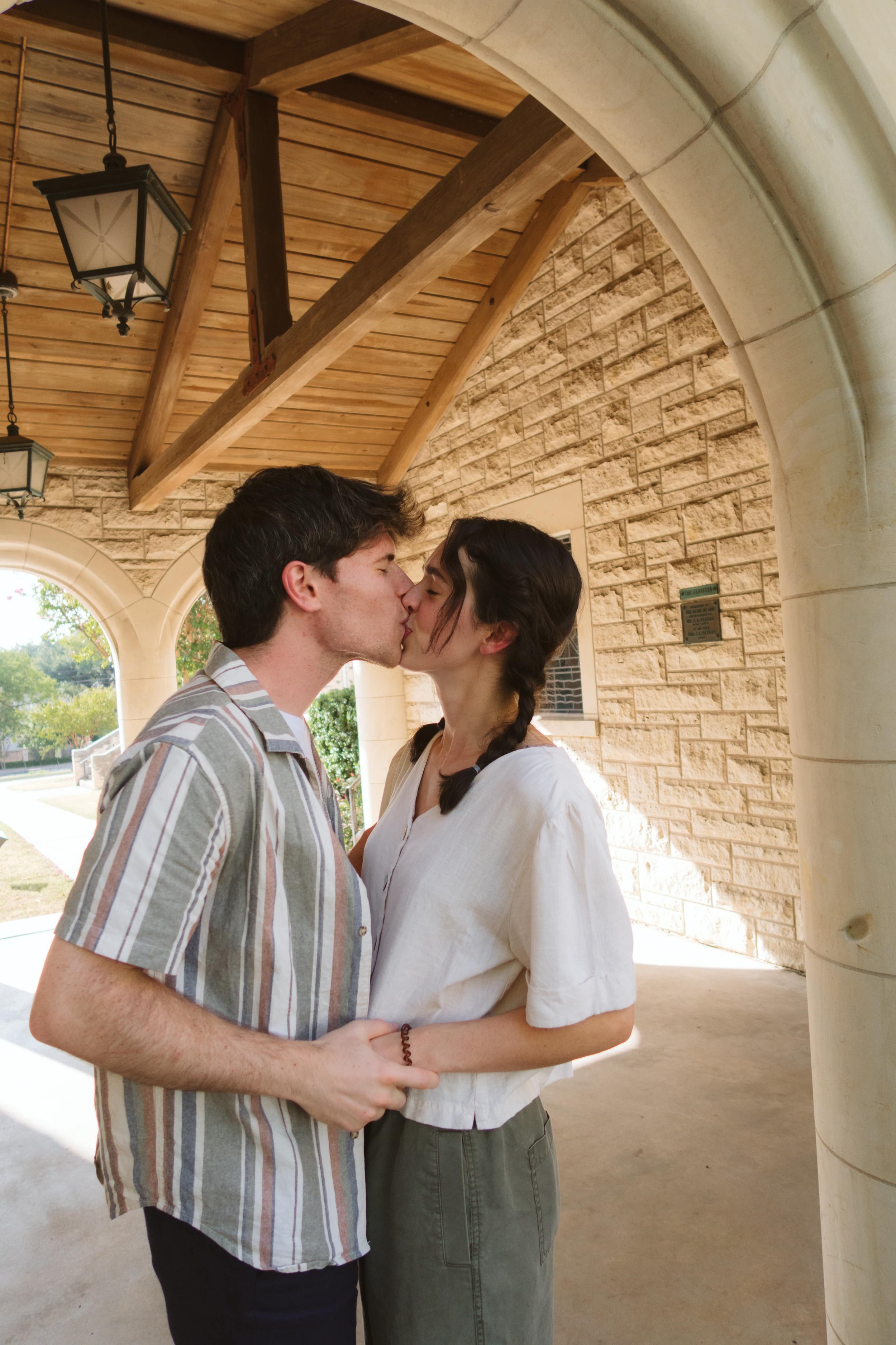 A young couple kissing under a wooden archway with arches in the background.
