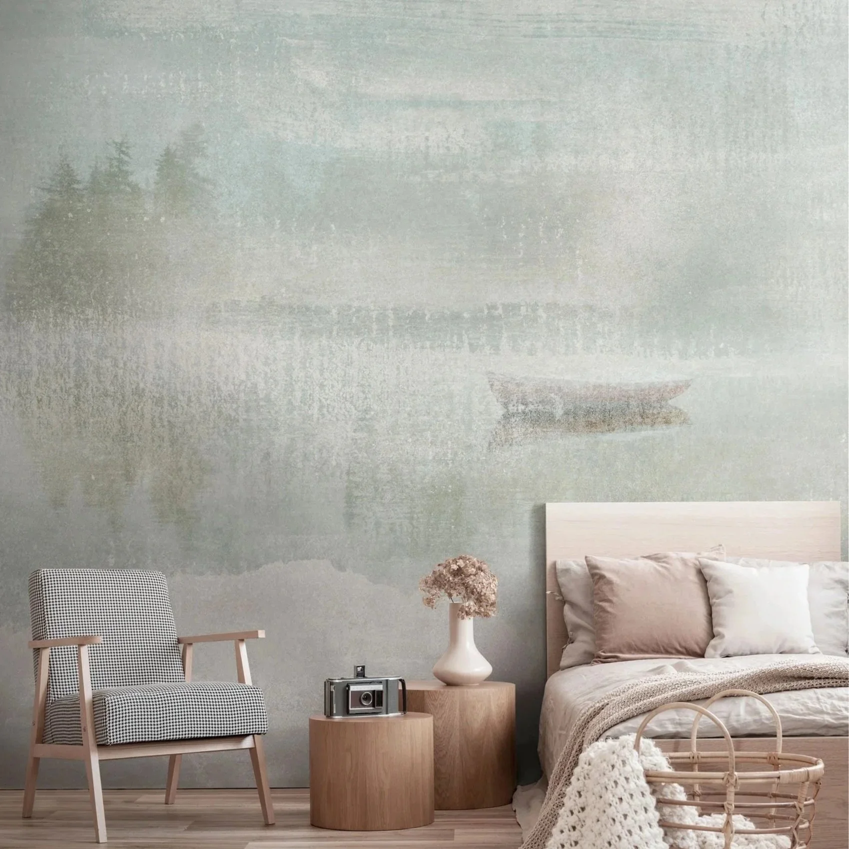 A bedroom with a textured wall depicting a misty lake scene with trees and a boat, a bed with neutral-colored pillows, a side table with a vase of flowers, a vintage camera, an armchair, and a woven basket.