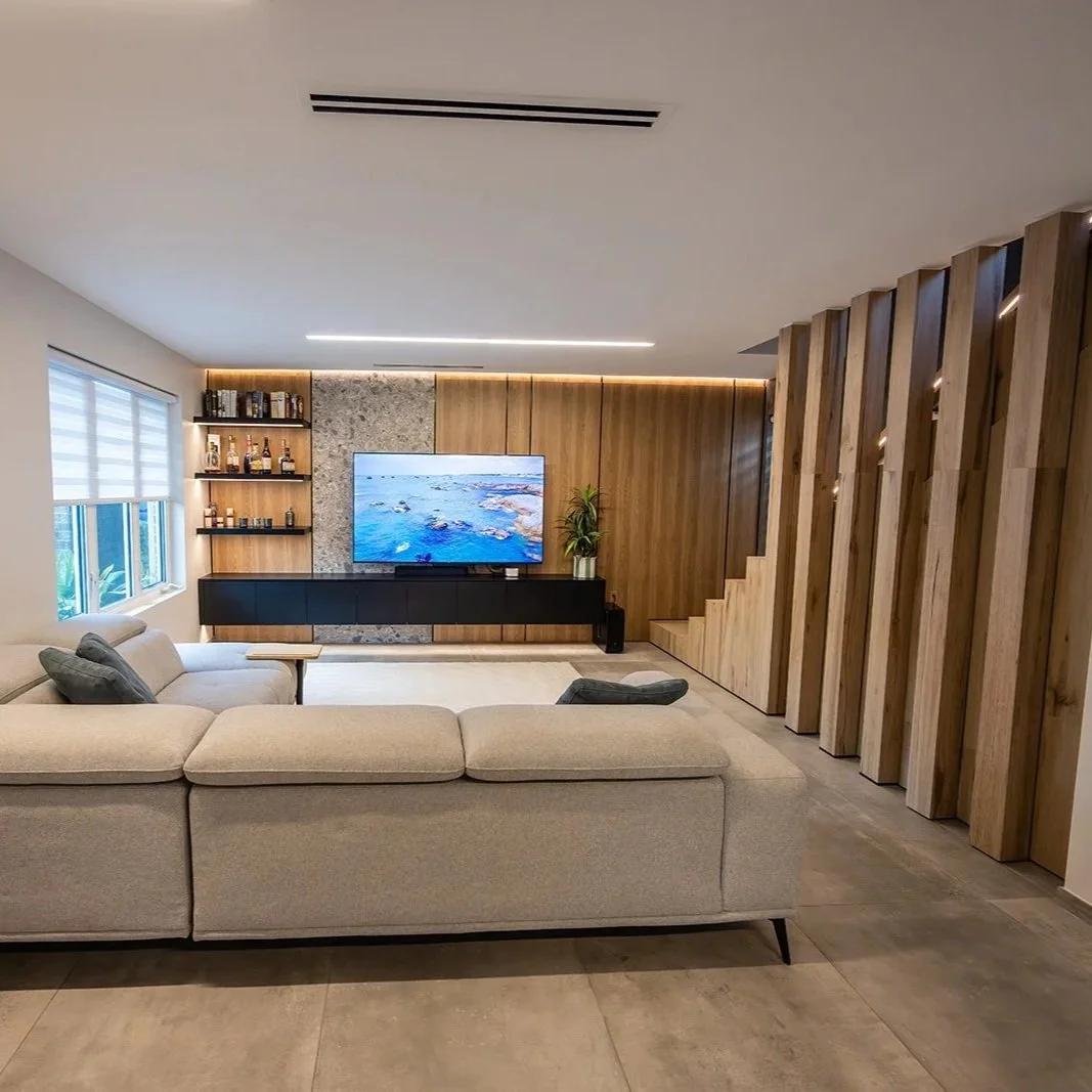 Open-plan luxury interior renovation showing modern living space with custom wood slat feature wall and designer furniture.