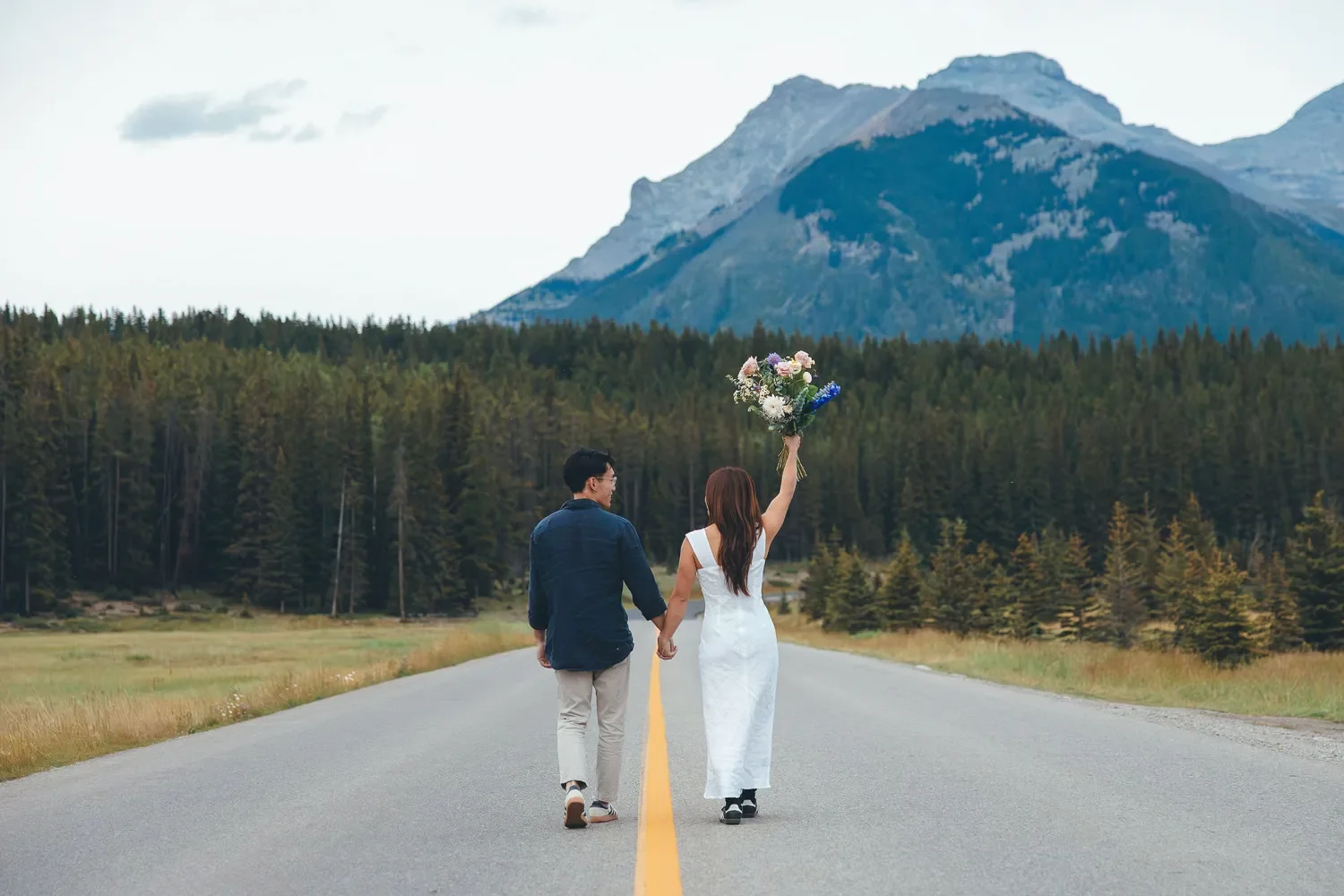 116_couple-walking-mountain-road-holding-bouquet-canadian-rockies.webp