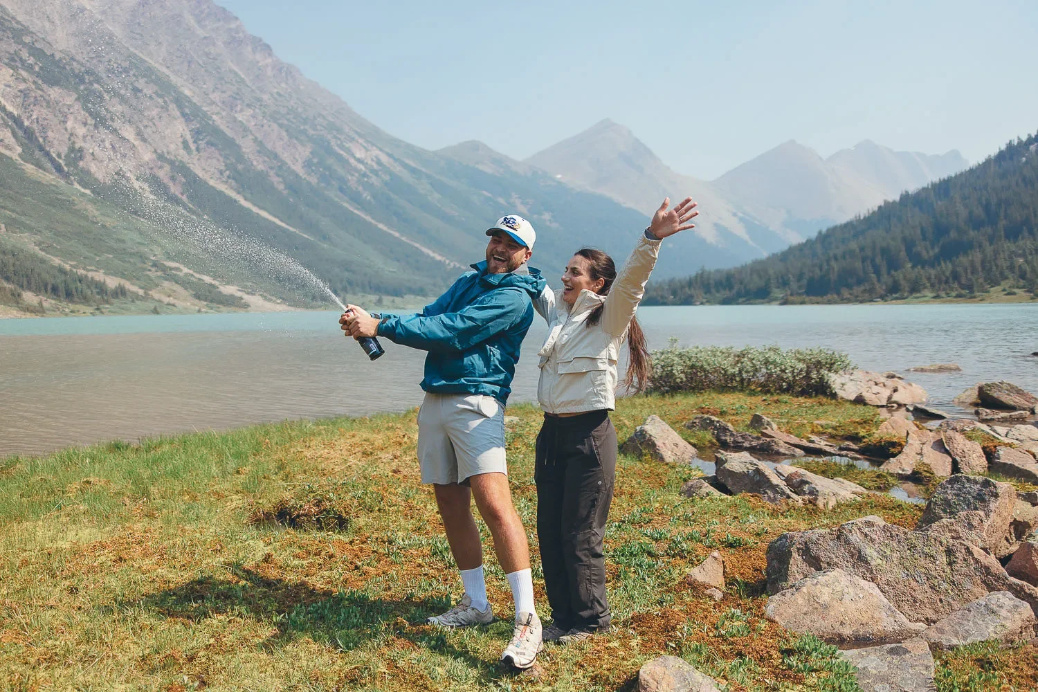 112_couple-celebrating-engagement-champagne-pop-alpine-lake-canadian-rockies.webp