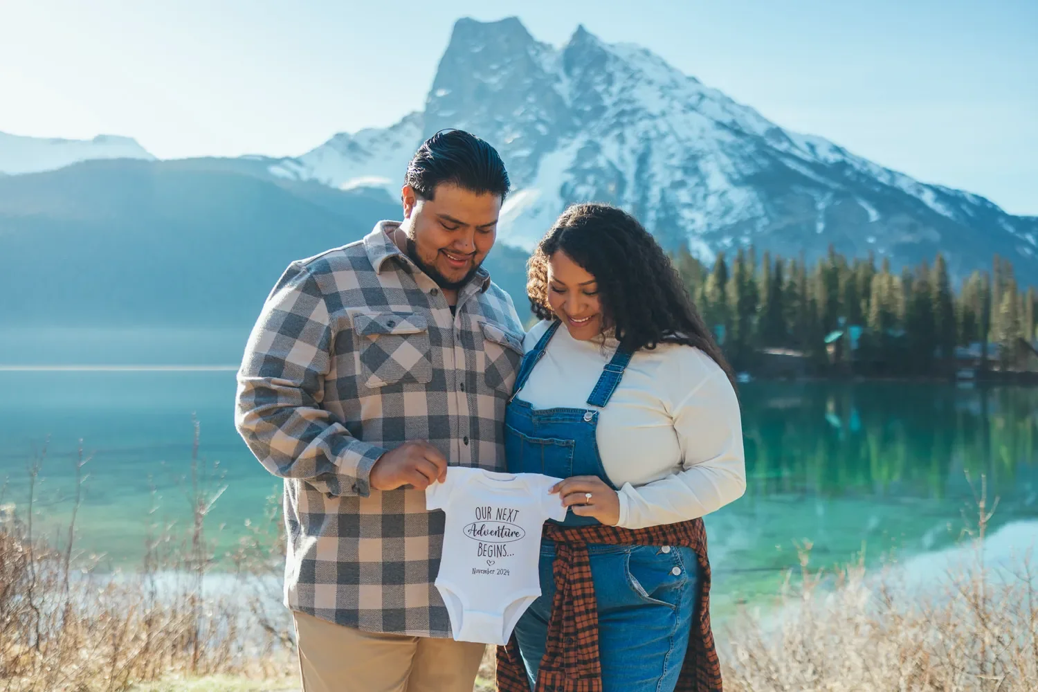 102_maternity-announcement-couple-holding-baby-onesie-emerald-lake-canadian-rockies.webp