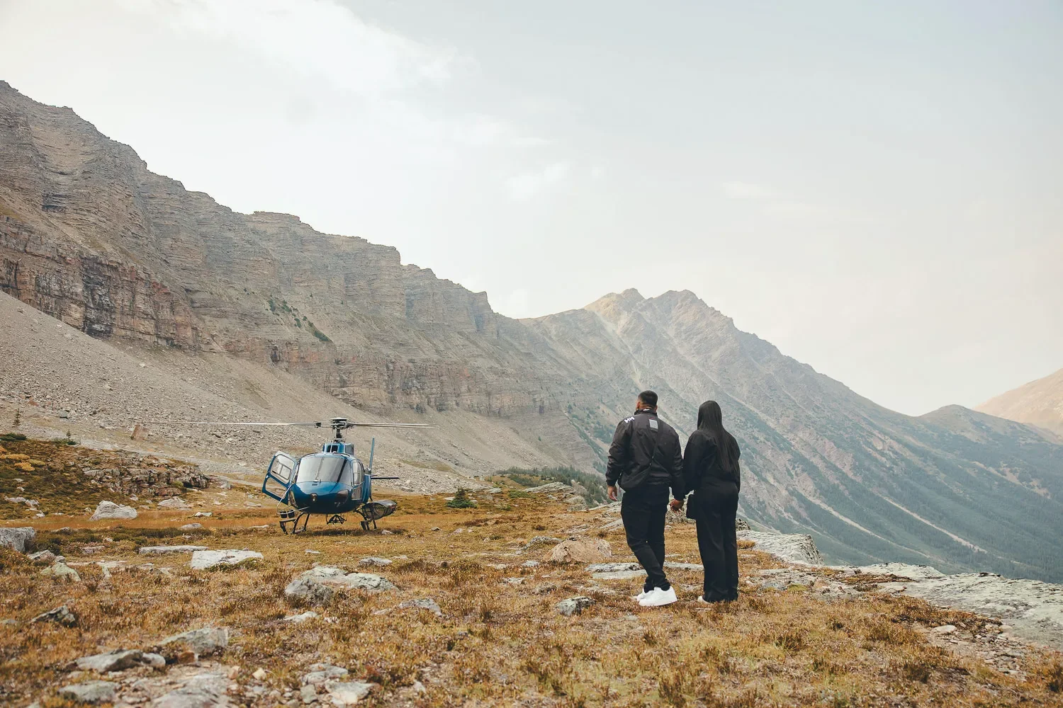 108_couple-walking-towards-blue-helicopter-mountain-landscape.webp