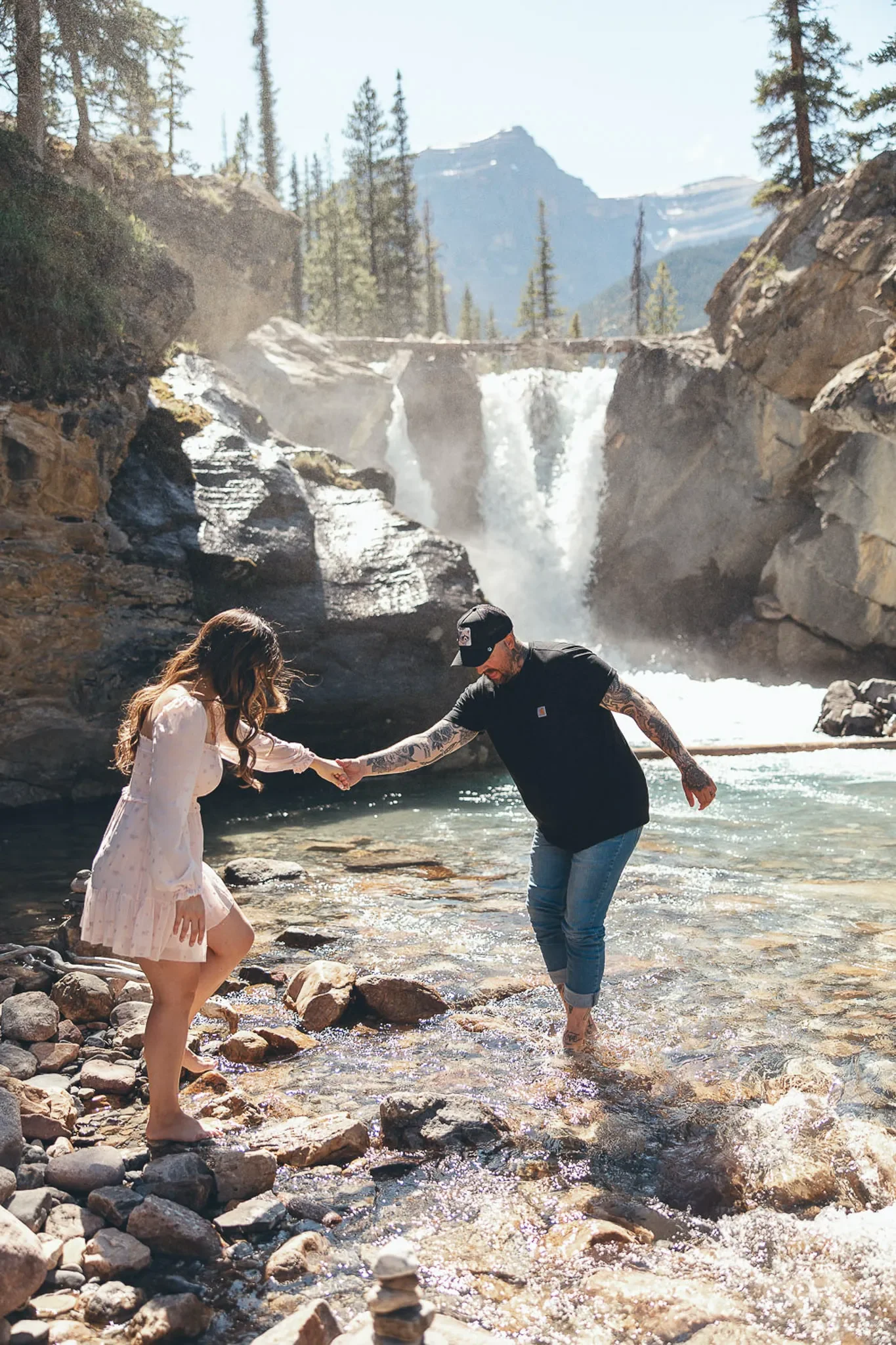 152_Couple-Walking-Crossing-Stream-Mountain-Waterfall-Canadian-Rockies.webp