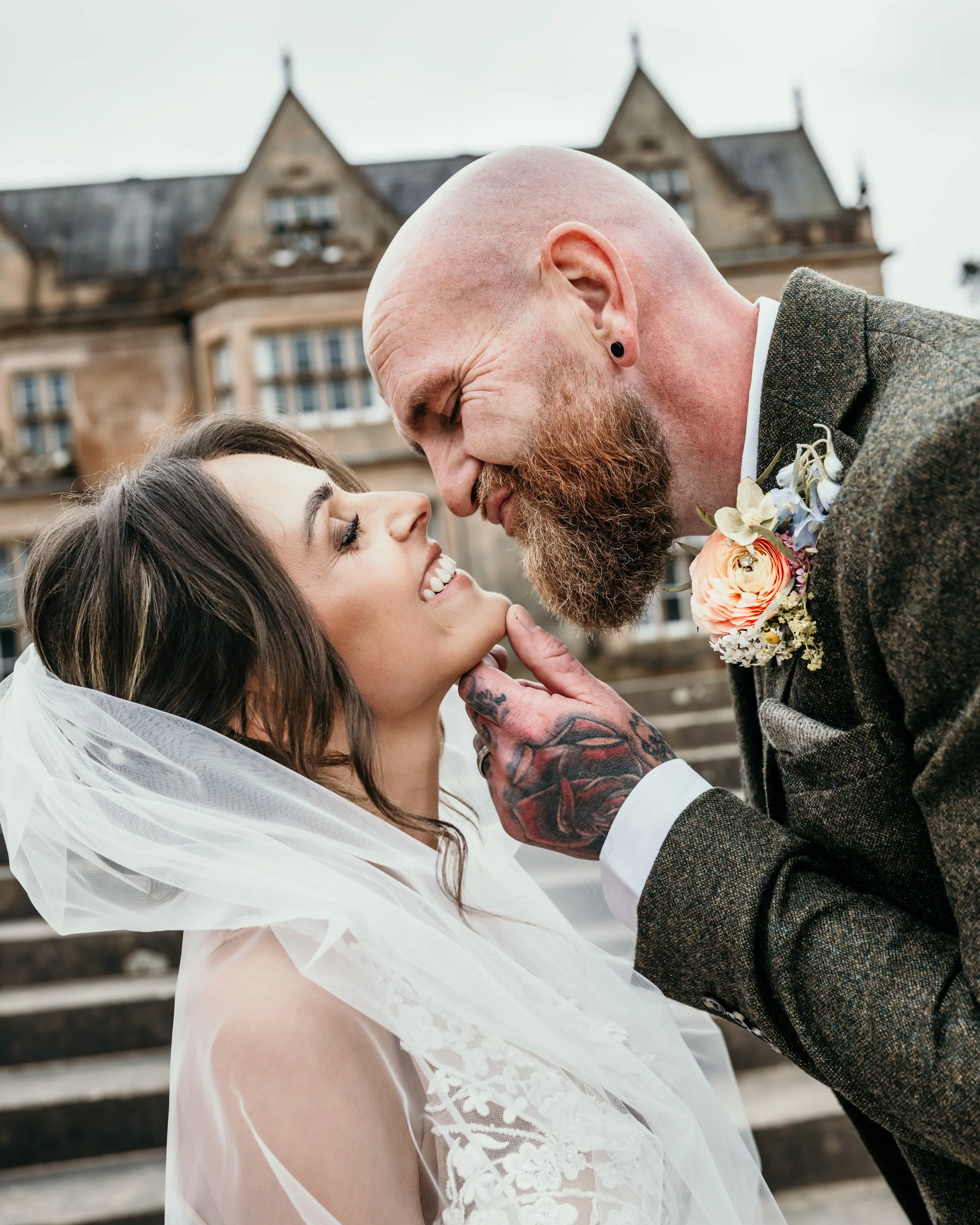 A bride and groom smile while the groom holds the bride's chin and leans in for a kiss.