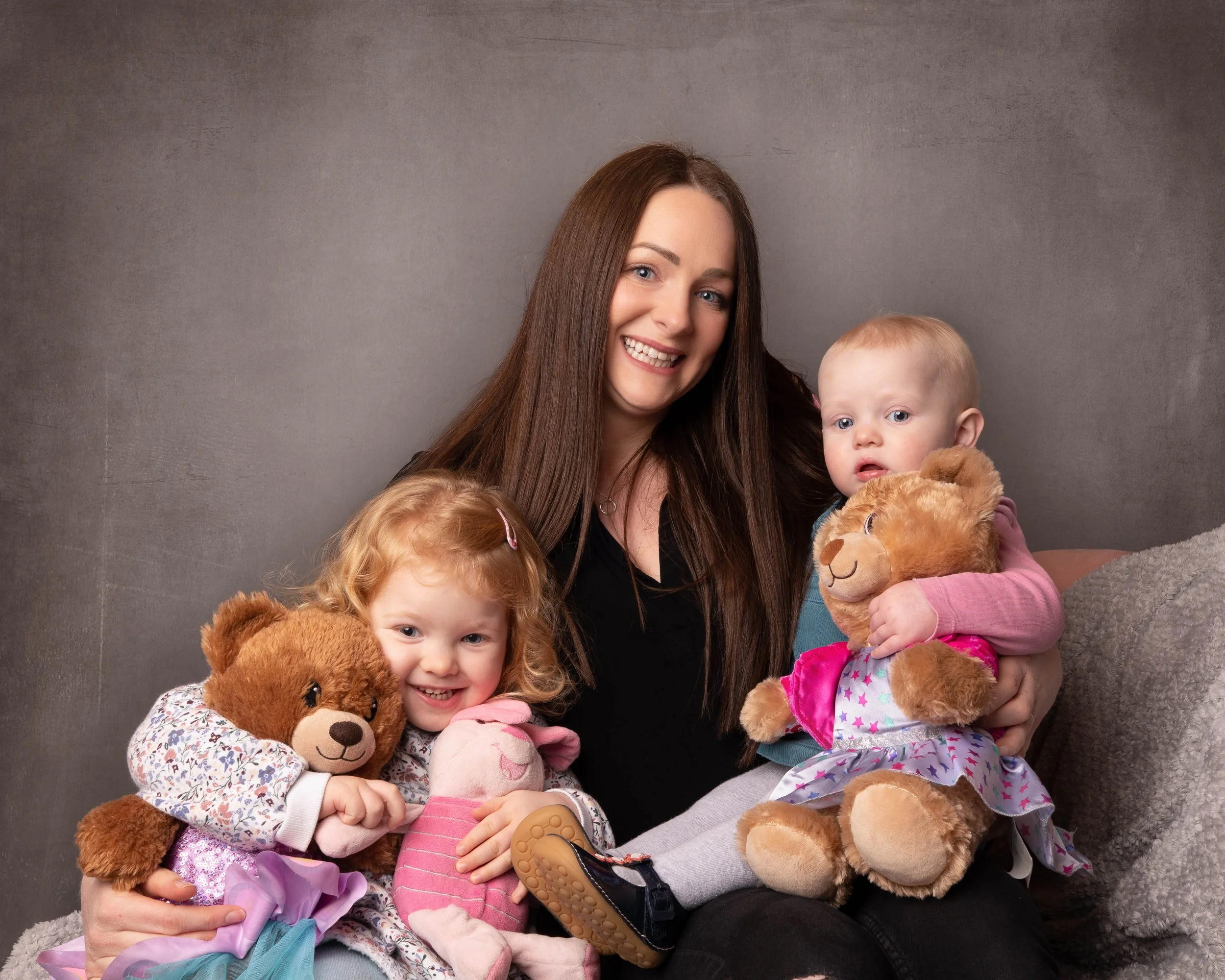 A mum hugs her two baby girls while they attend a family photoshoot in a photography studio in Ballynahinch