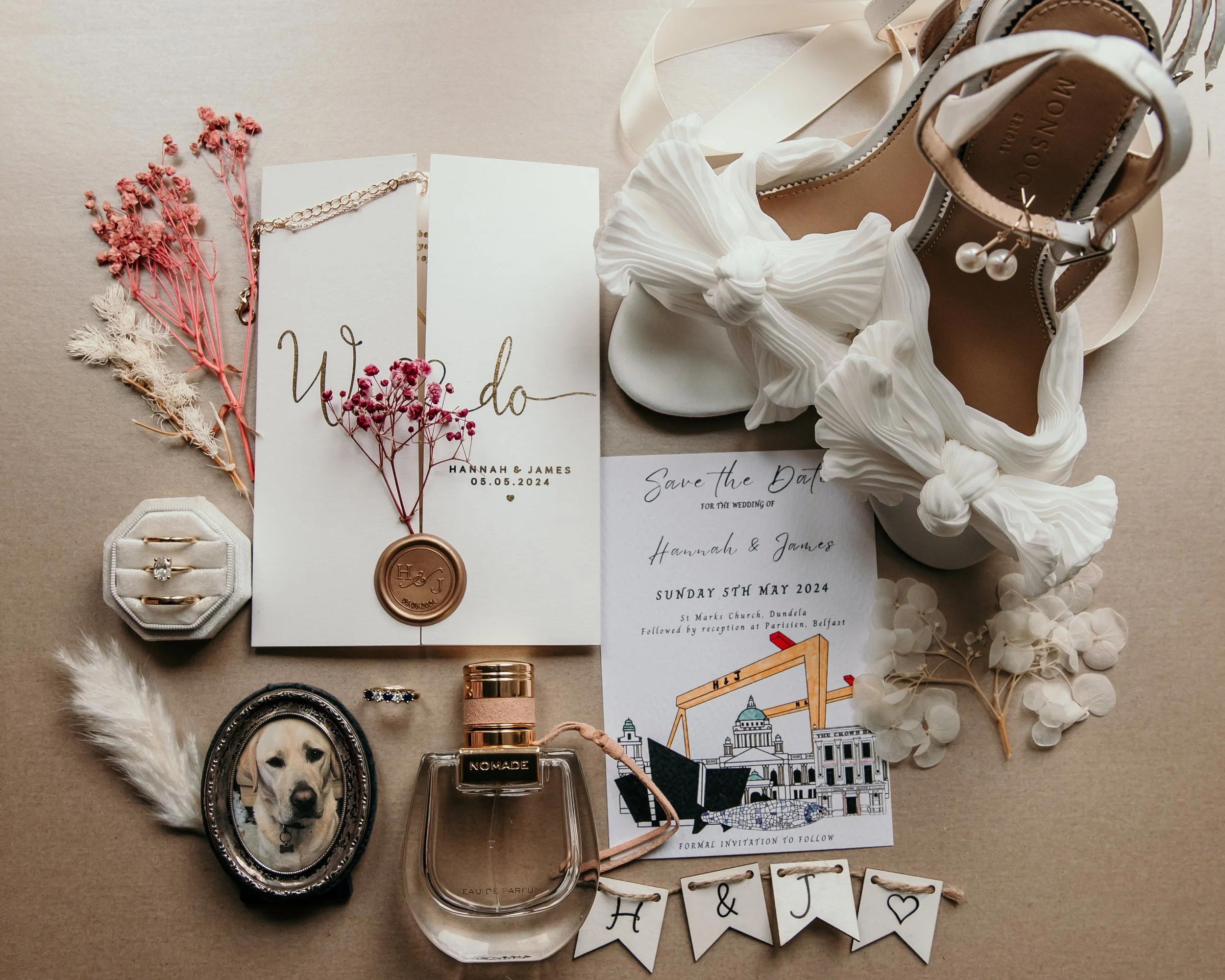 Flat lay image of wedding shoes, perfume, wedding earrings, wedding day invite, engagement ring, wedding ring