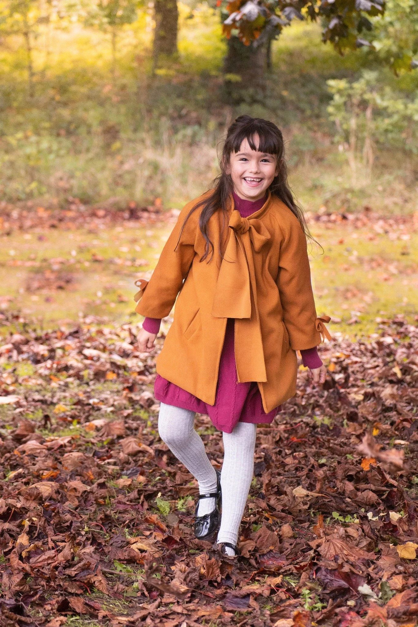 Girl is laughing into the camera and having fun playing in the autumn leaves in the woods.