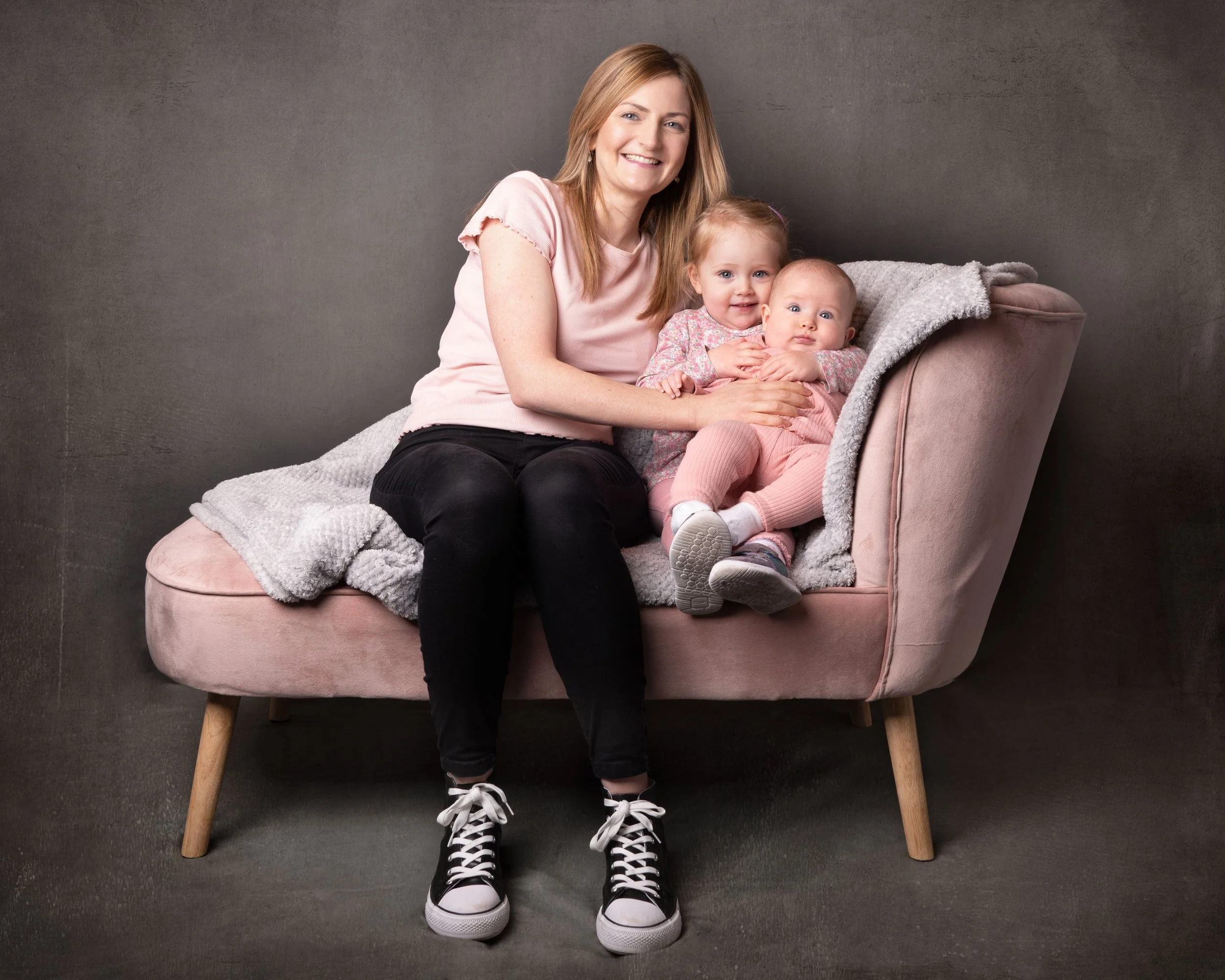 A Mum and her 2 daughters sit on a chair and smile for a family photo in the Ballynahinch studio