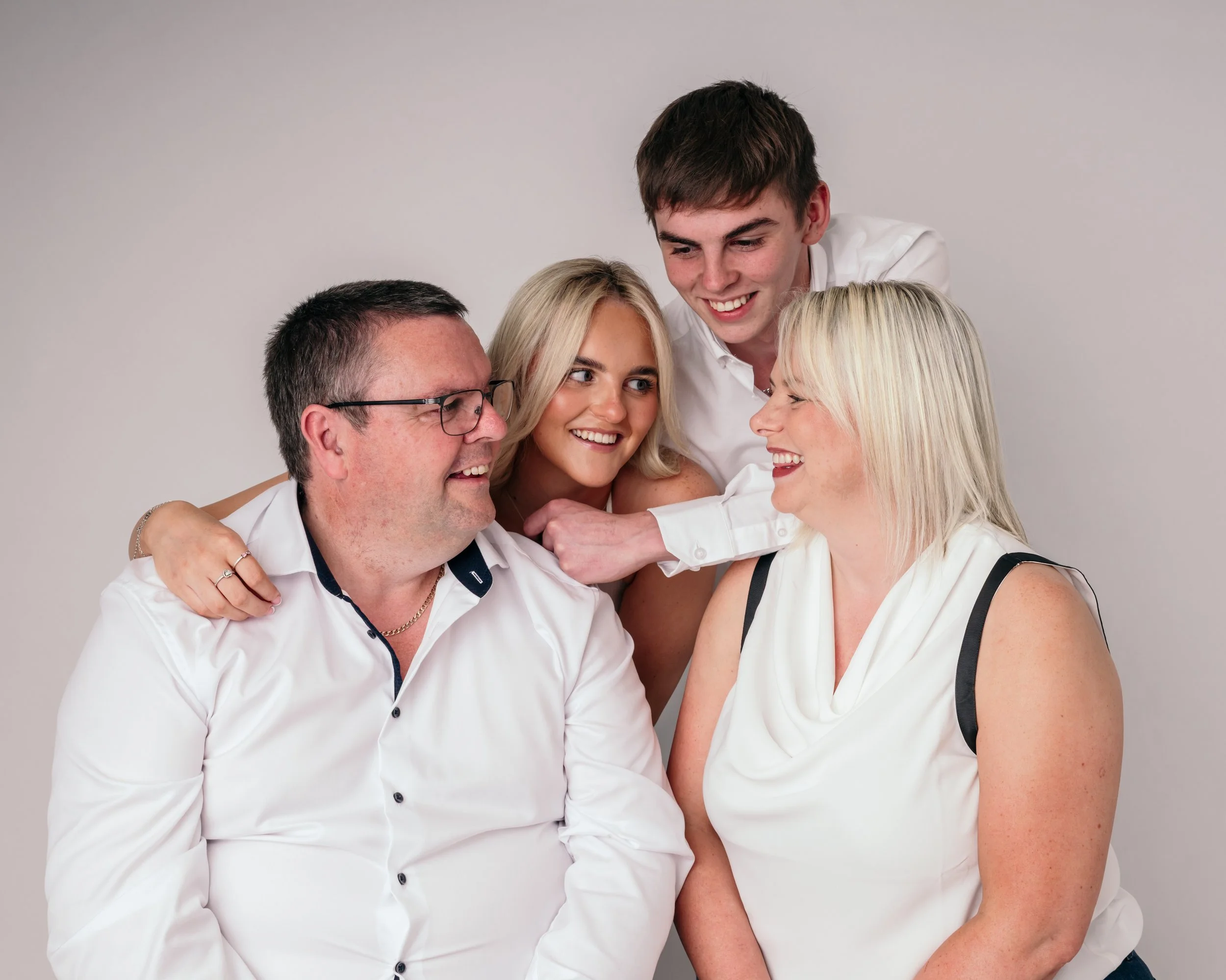 Group of five people, three women and two men, smiling and embracing each other against a neutral gray background.