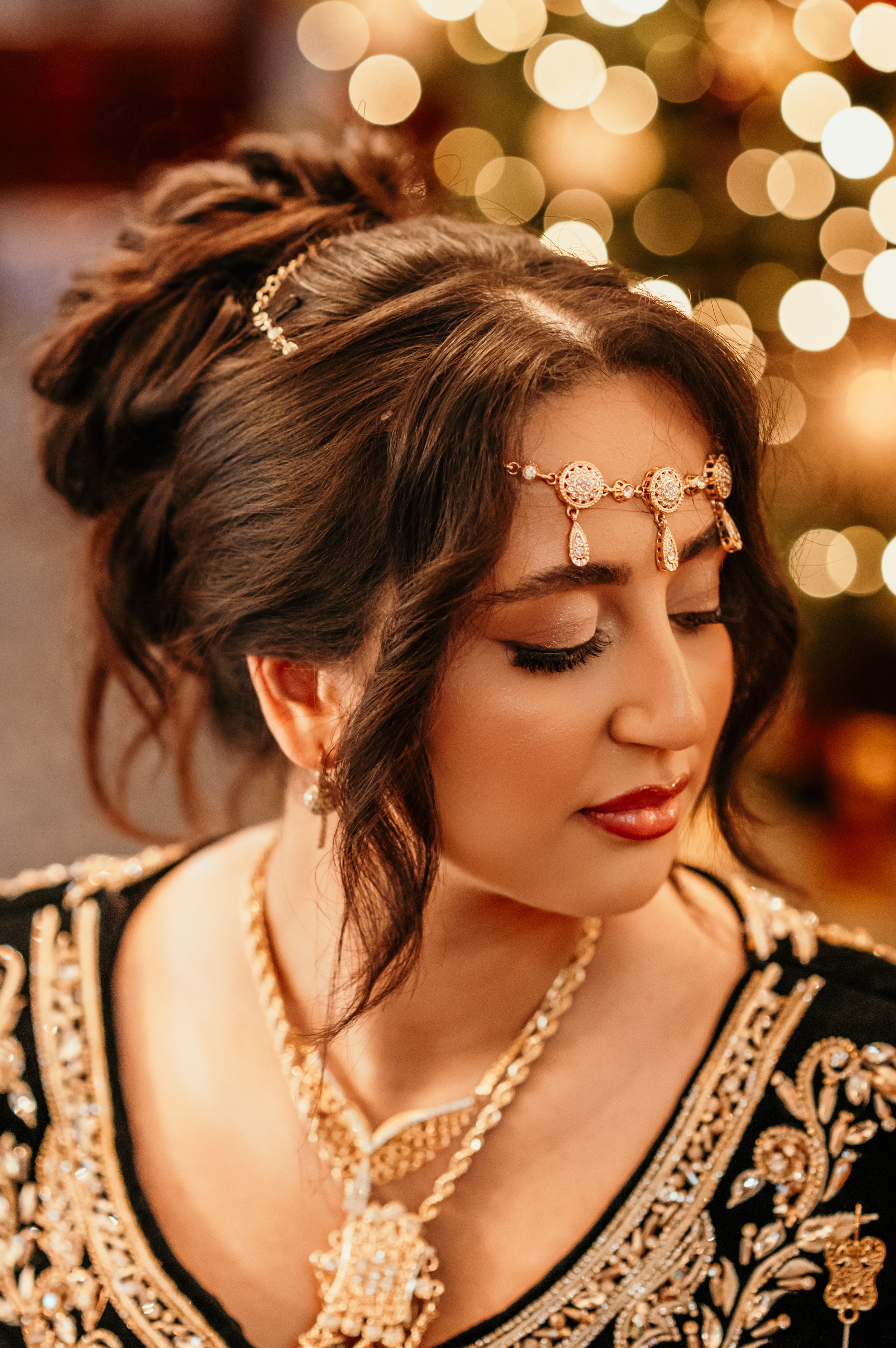 An Algerian Bride turns her head away from the camera and looks downward. She wears a traditional black and gold Algerian wedding outfit and headdress.