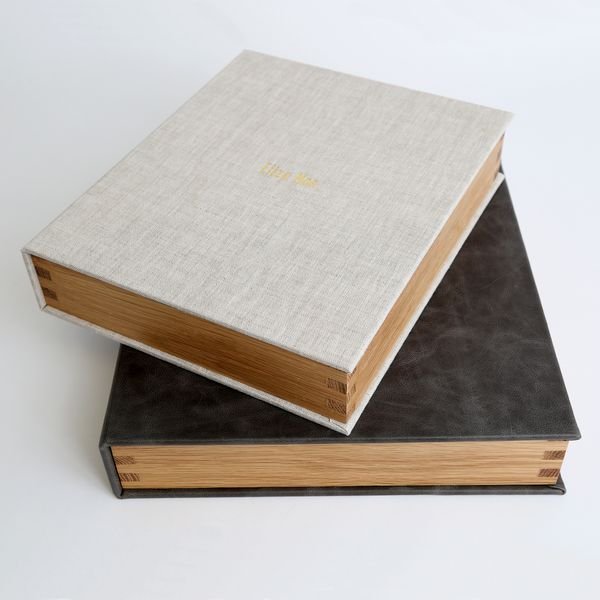 Two stacked closed photo albums, one with a beige cover and one with a dark cover, on a light background.
