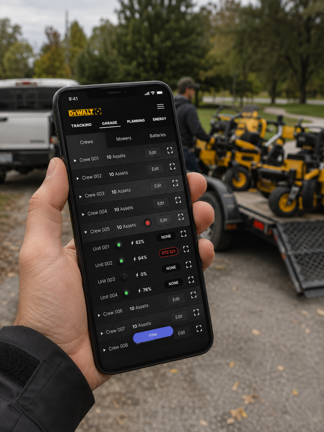 Person holding smartphone with DeWalt app monitoring power tool batteries, with construction equipment and a worker in the background.
