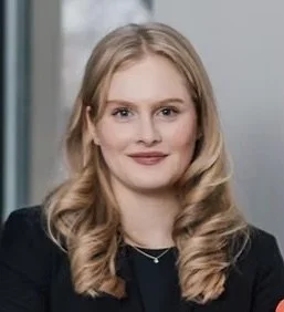 Portrait of a young woman with blonde hair, wearing a black blazer, smiling.