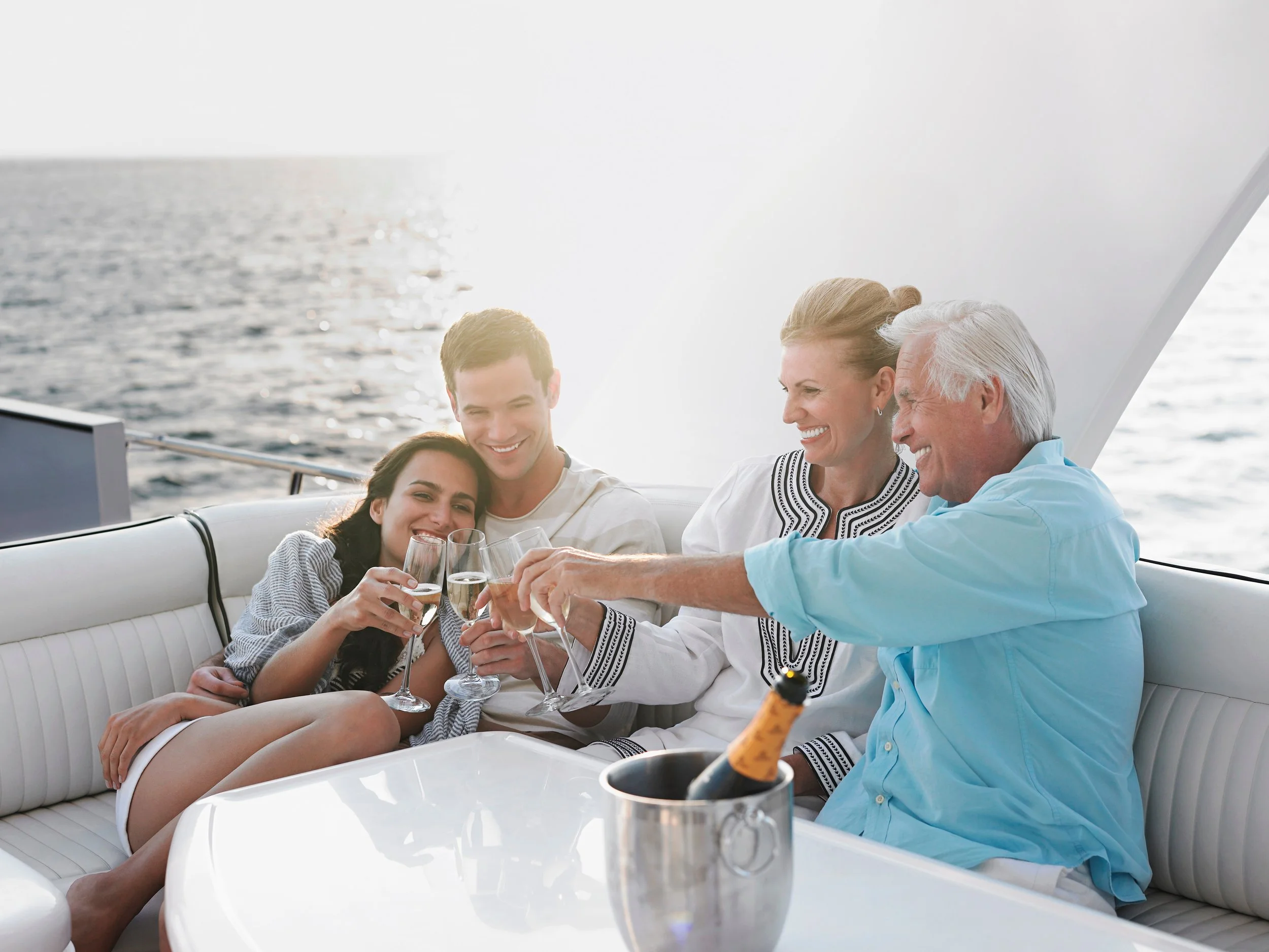 Four people celebrating with champagne on a yacht, smiling and toasting, with the ocean in the background.
