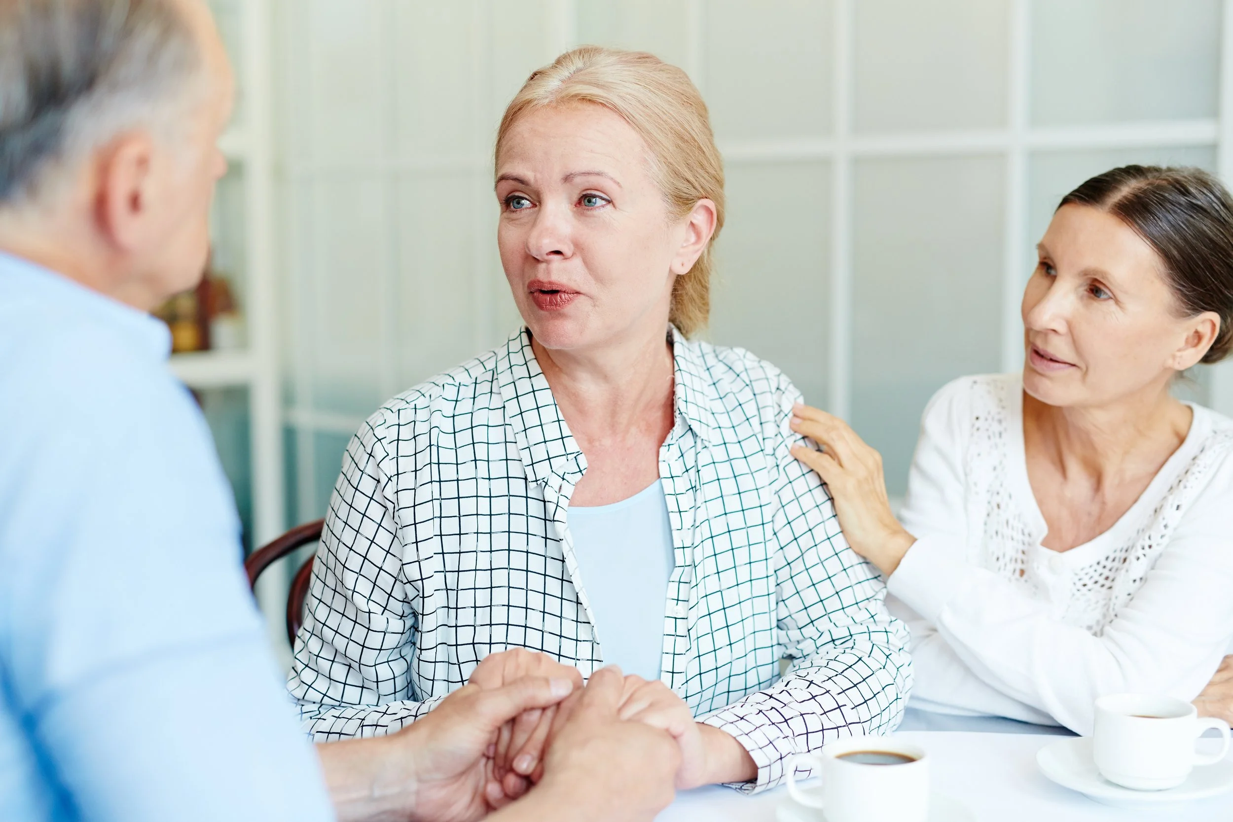 Three people having a serious conversation at a table with cups of coffee.
