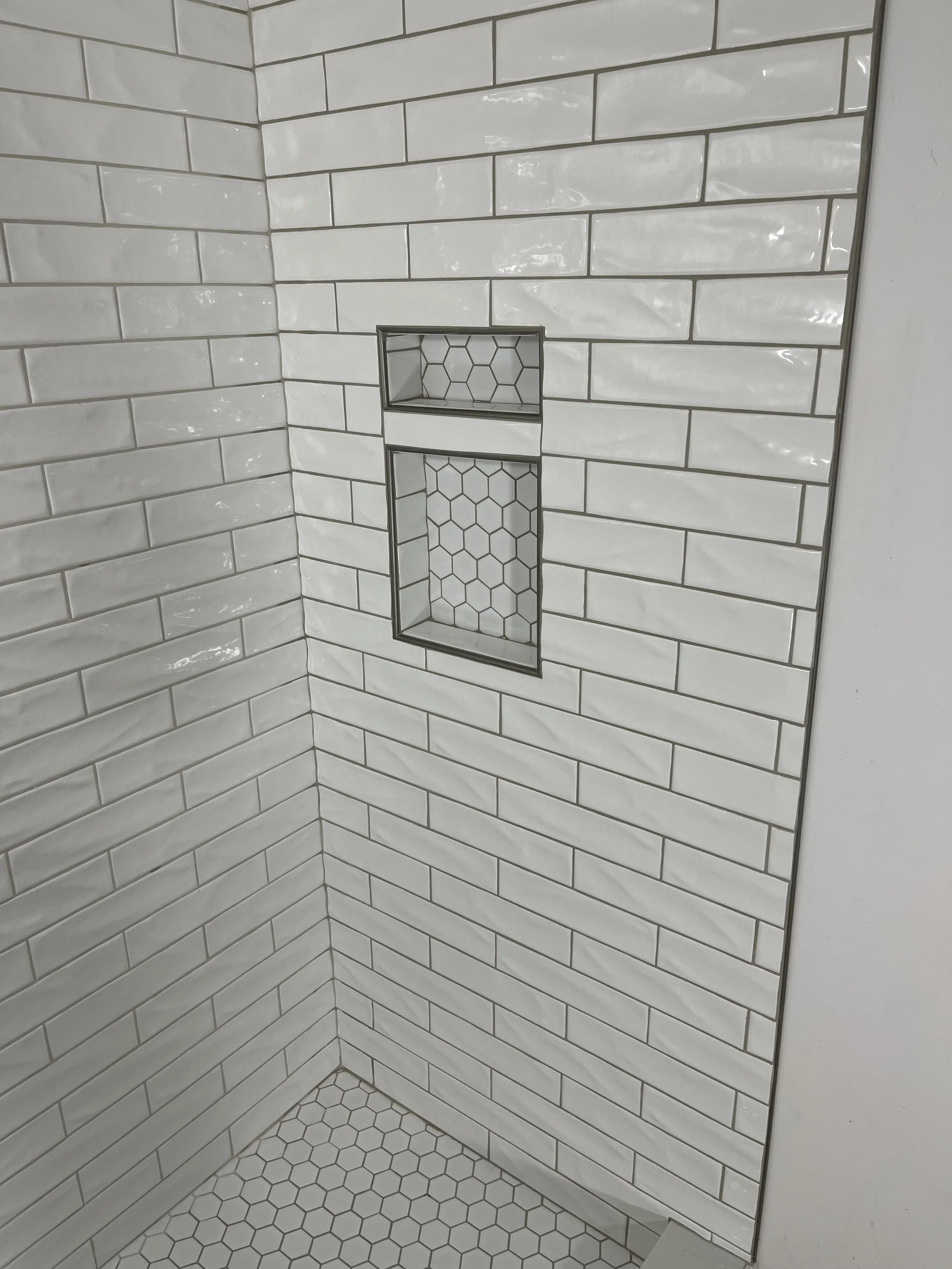 Corner of a tiled shower with white subway tiles and a built-in niche with hexagonal tile accents.