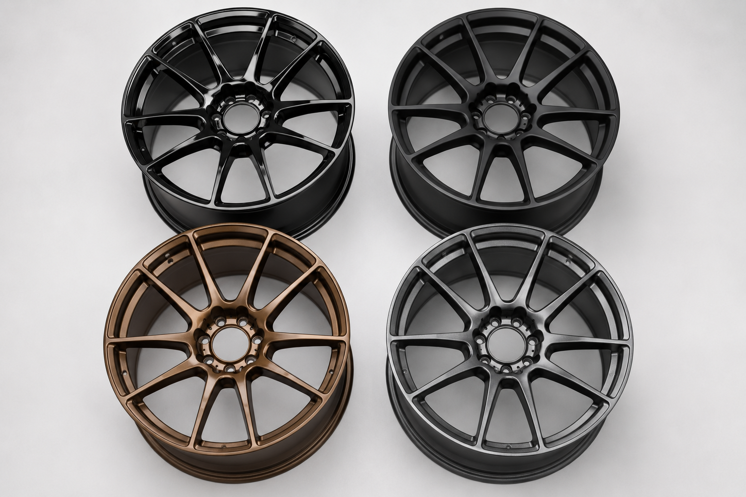 Four aftermarket car wheels displayed in a studio, showcasing gloss black, matte black, bronze metallic, and gunmetal grey powder coating finishes.