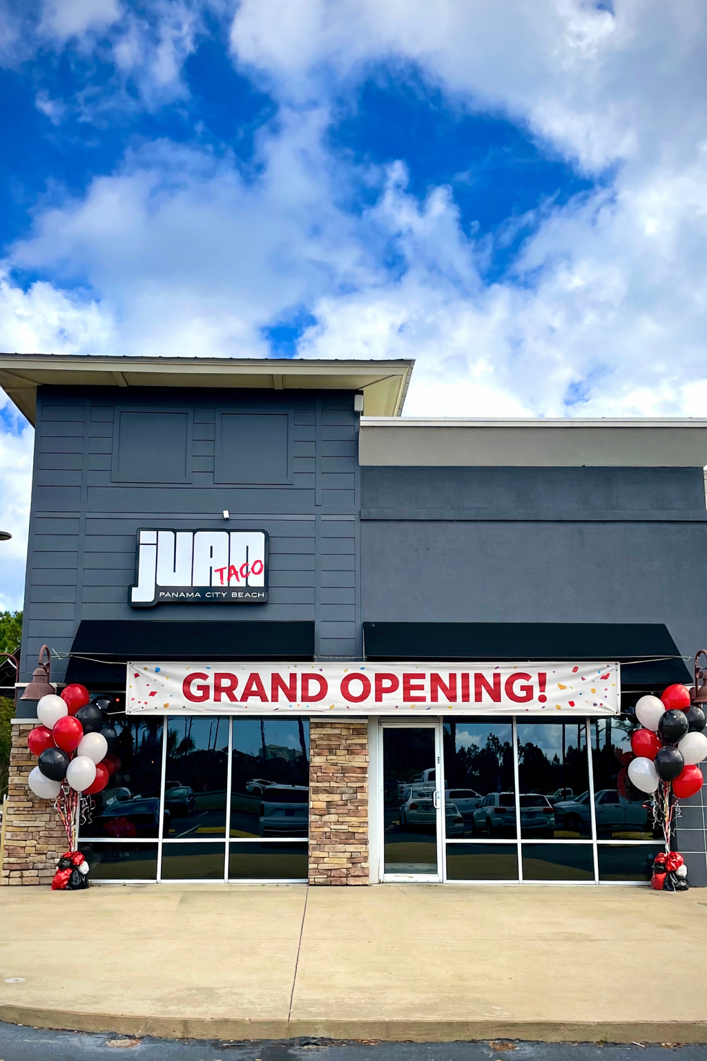 The exterior of Jabo Taco restaurant with a grand opening banner, balloons, and a cloudy blue sky.