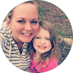 A woman and a young girl smiling outdoors, with trees in the background.