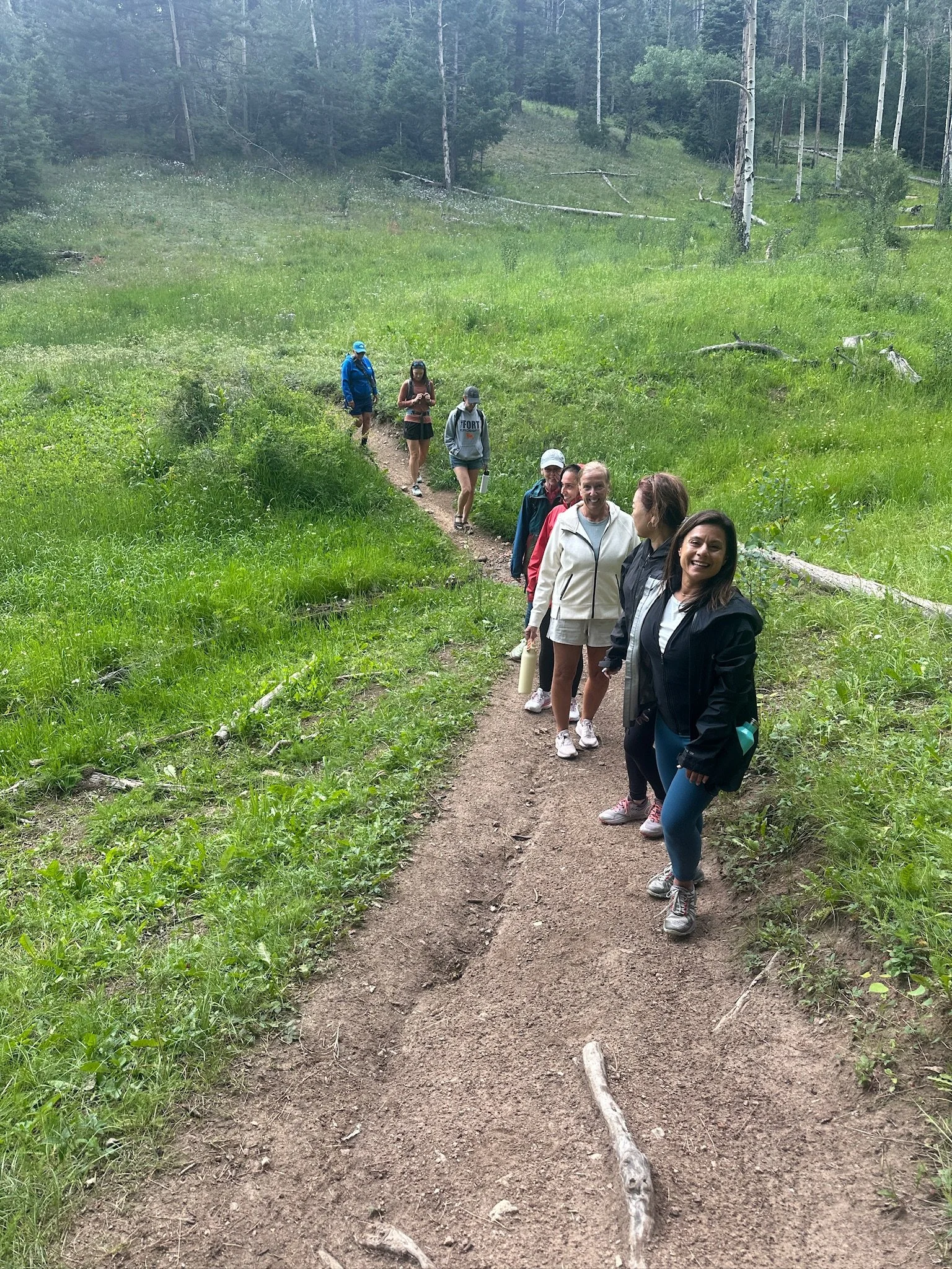 A group of people walking along a dirt trail through a lush green forest in the daytime.