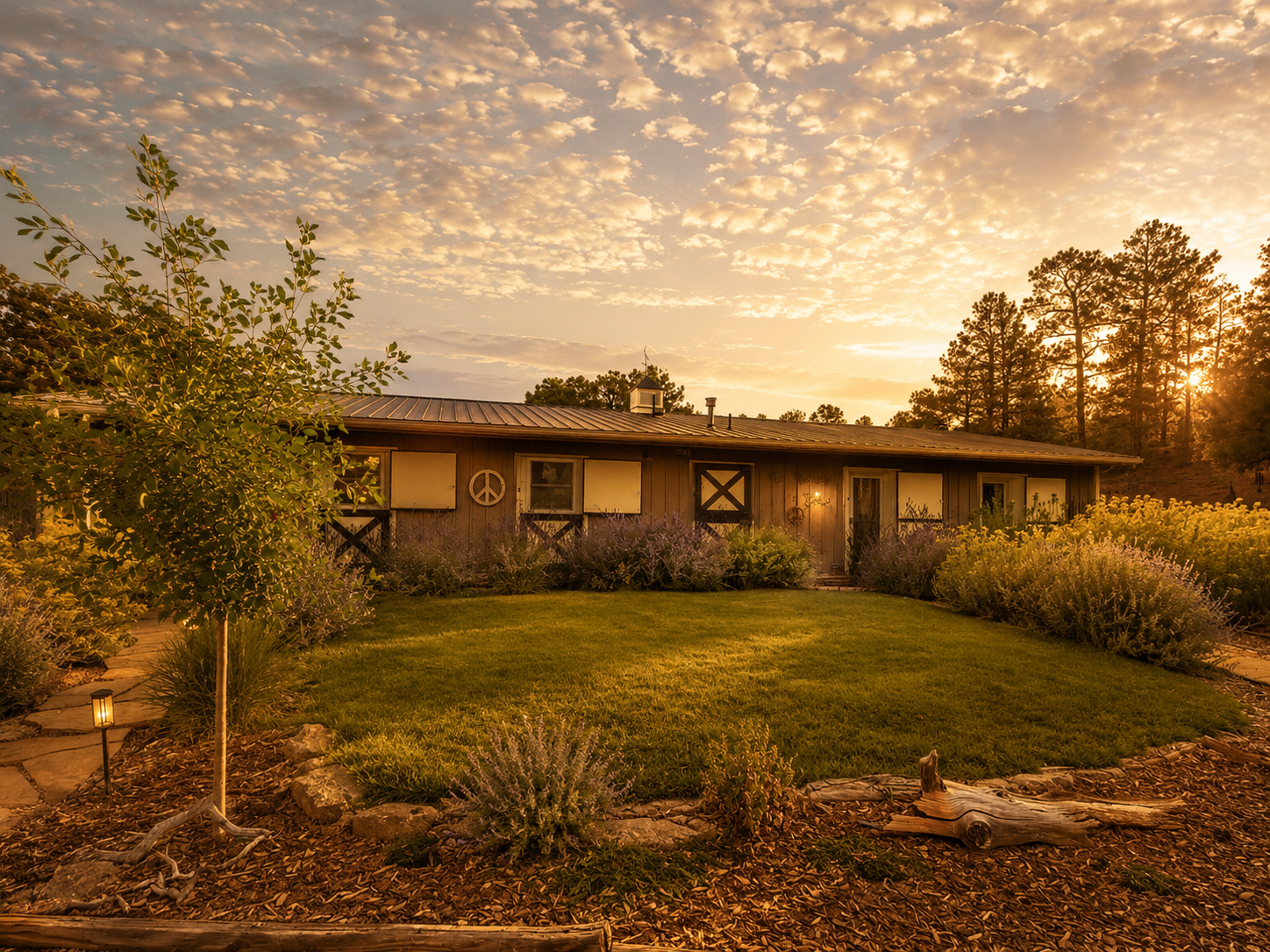 A rustic house during sunset with a well-maintained lawn, surrounded by flowering bushes and trees, and a lantern lighting the garden pathway.