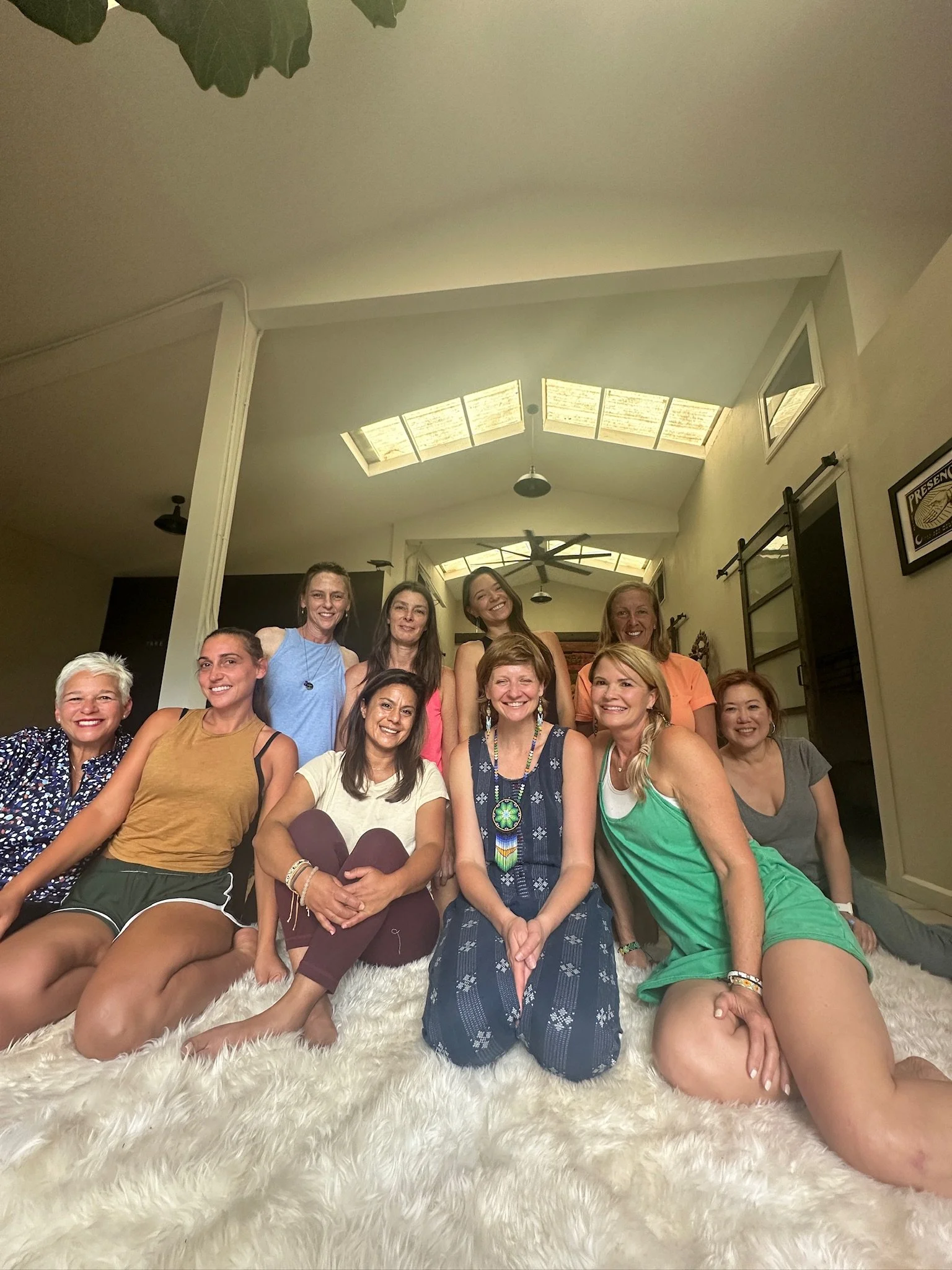 Group of women sitting and standing on a fluffy rug inside a home, smiling at the camera.
