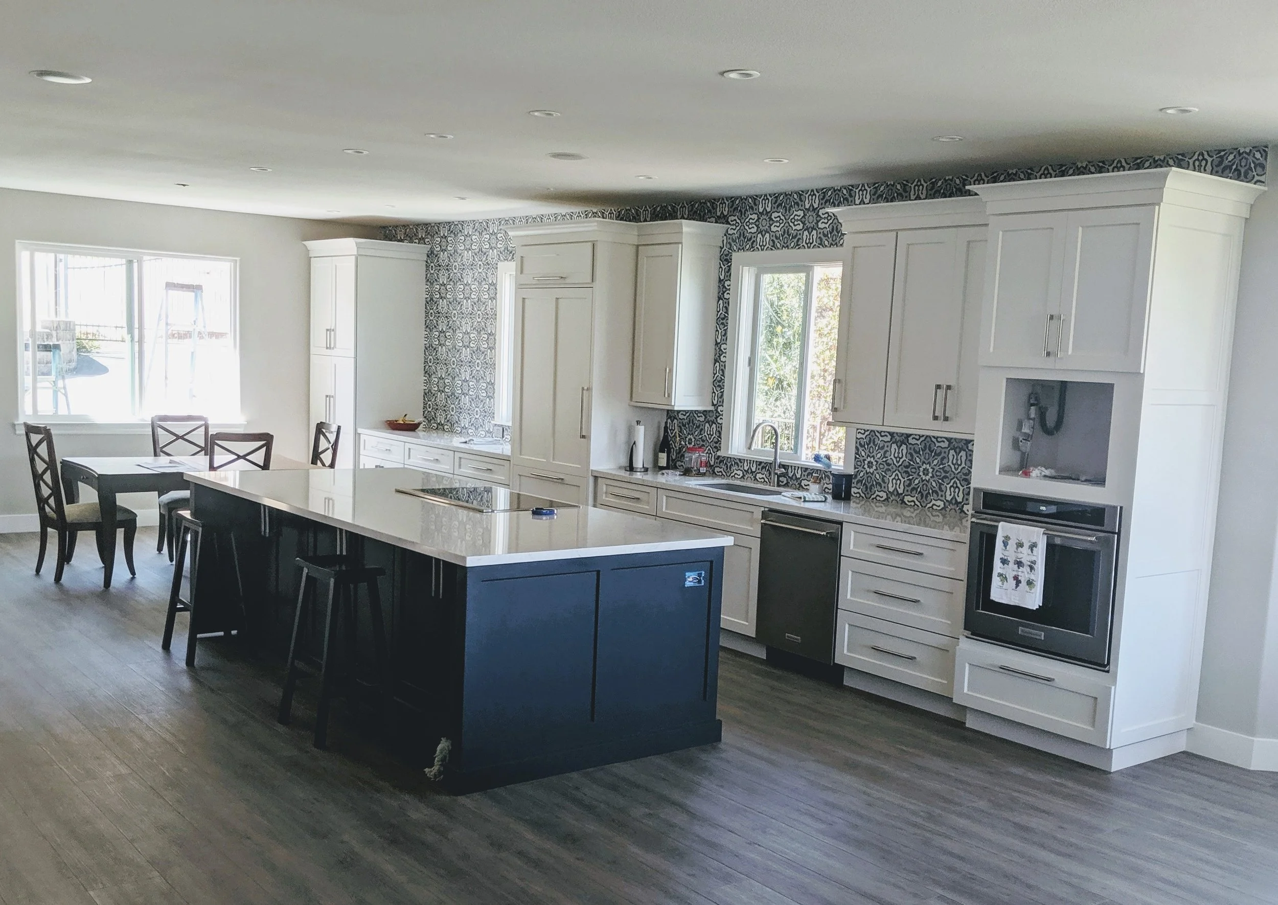 Whole Home Remodeling Contractor in Atascadero, CA. Modern kitchen with white cabinetry, black kitchen island, patterned wallpaper, and large windows.