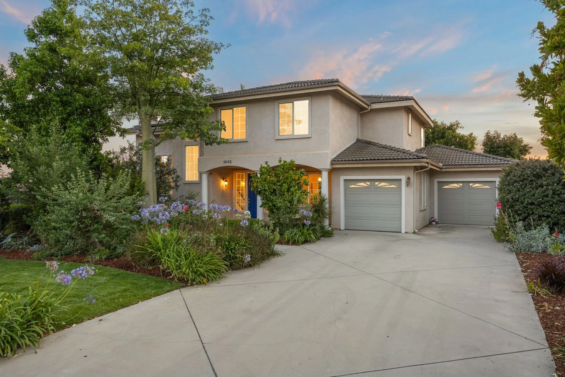 A two-story suburban house with attached garage, front yard, and landscaping during sunset.