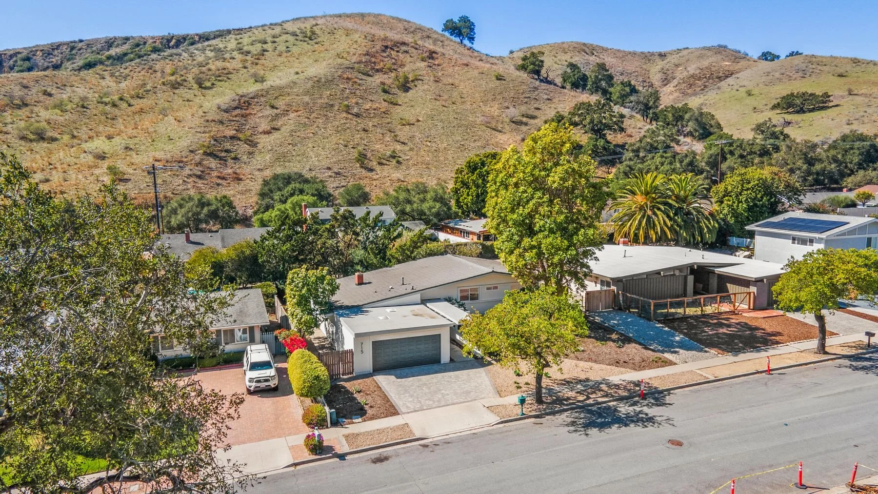 Aerial view of a residential neighborhood with single-story houses, trees, and a mountain in the background.