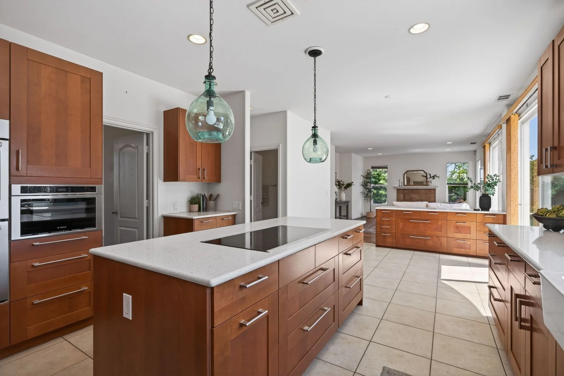 Modern kitchen with wooden cabinets, white countertops, built-in oven, and large windows with natural light.