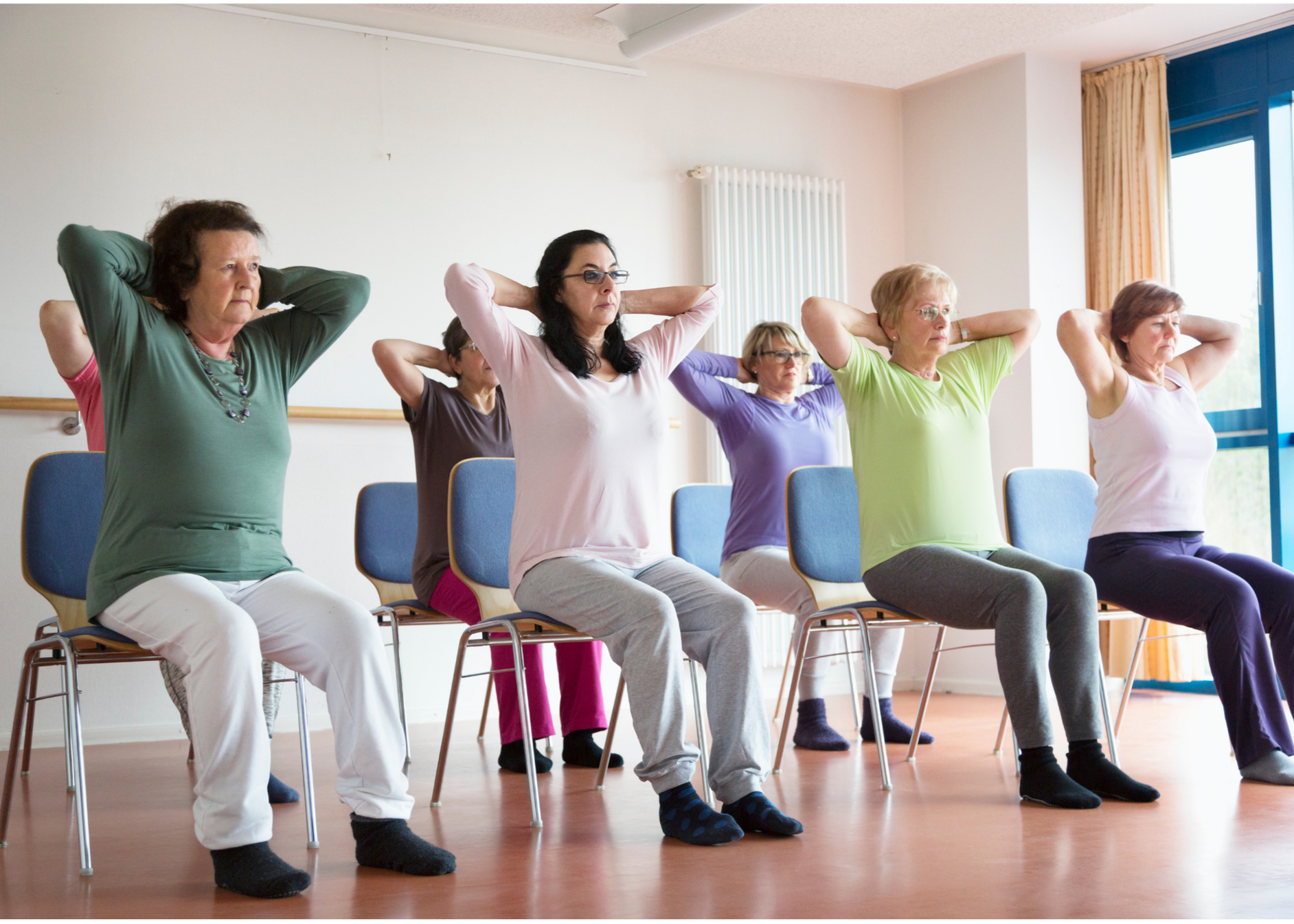 Chair Yoga class with seven women sitting upright in chairs and their hands clasped behind their heads
