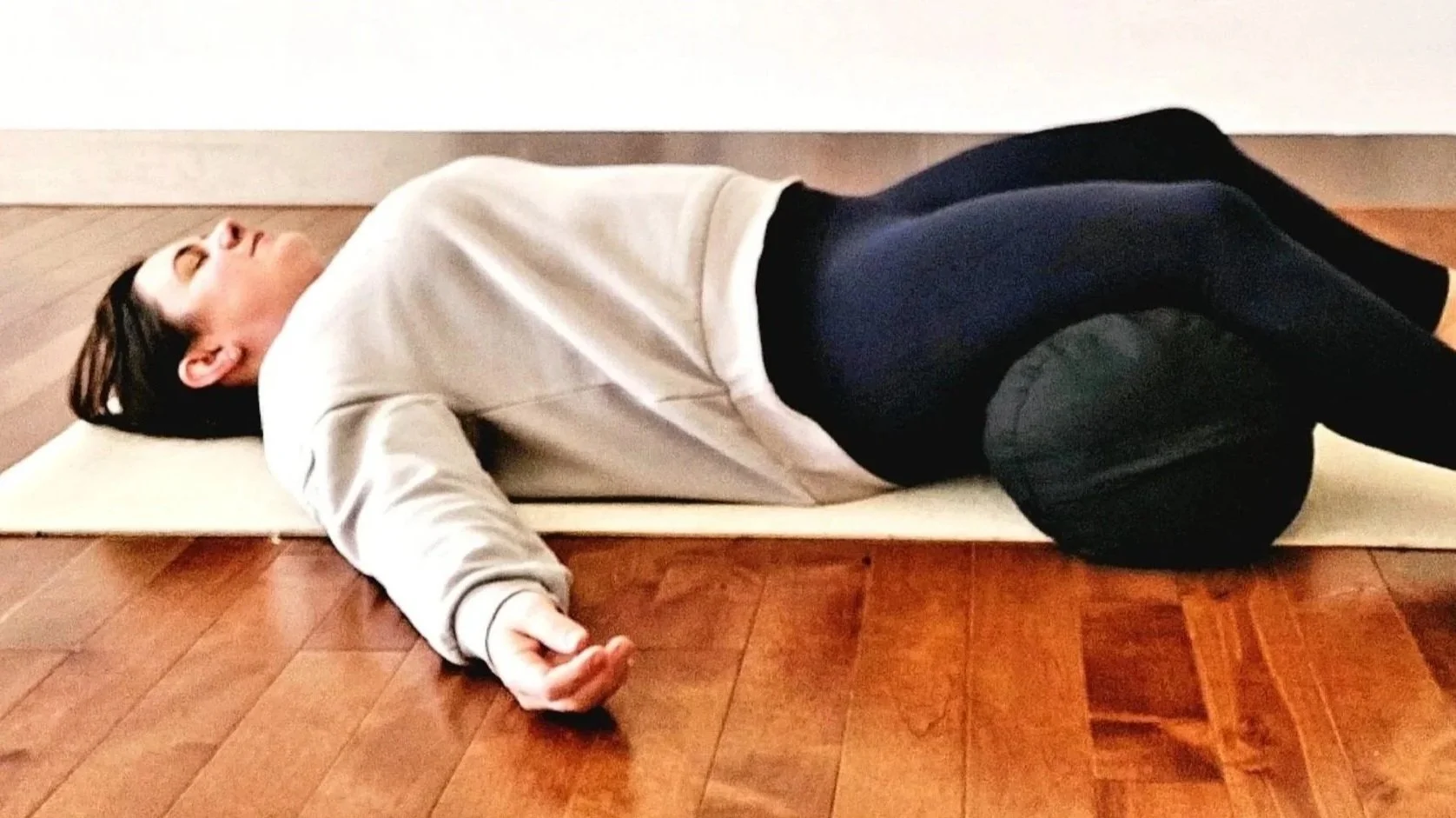 Woman lying on back in Yin yoga Savasana position with a bolster under the legs