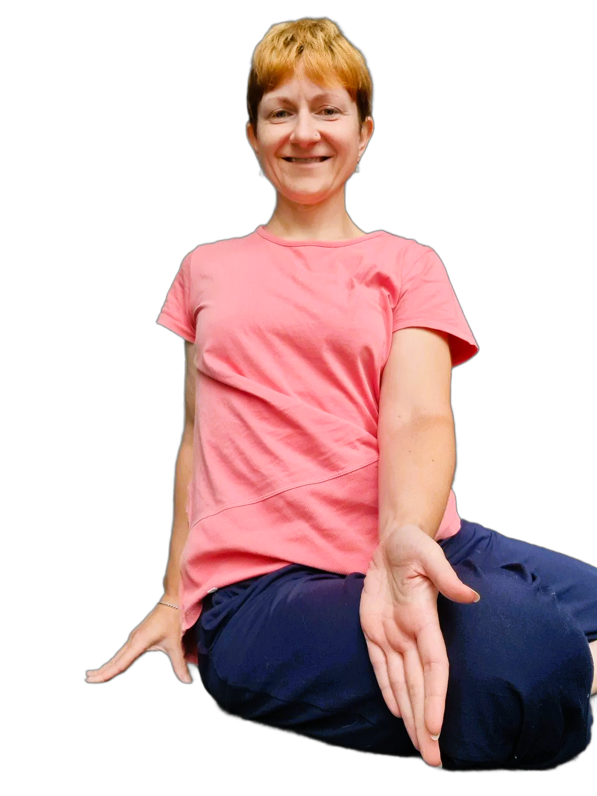 Woman wearing a pink shirt and navy pants in a yoga pose with legs bent to the side and a twist through the body, one hand on the thigh, looking at the camera