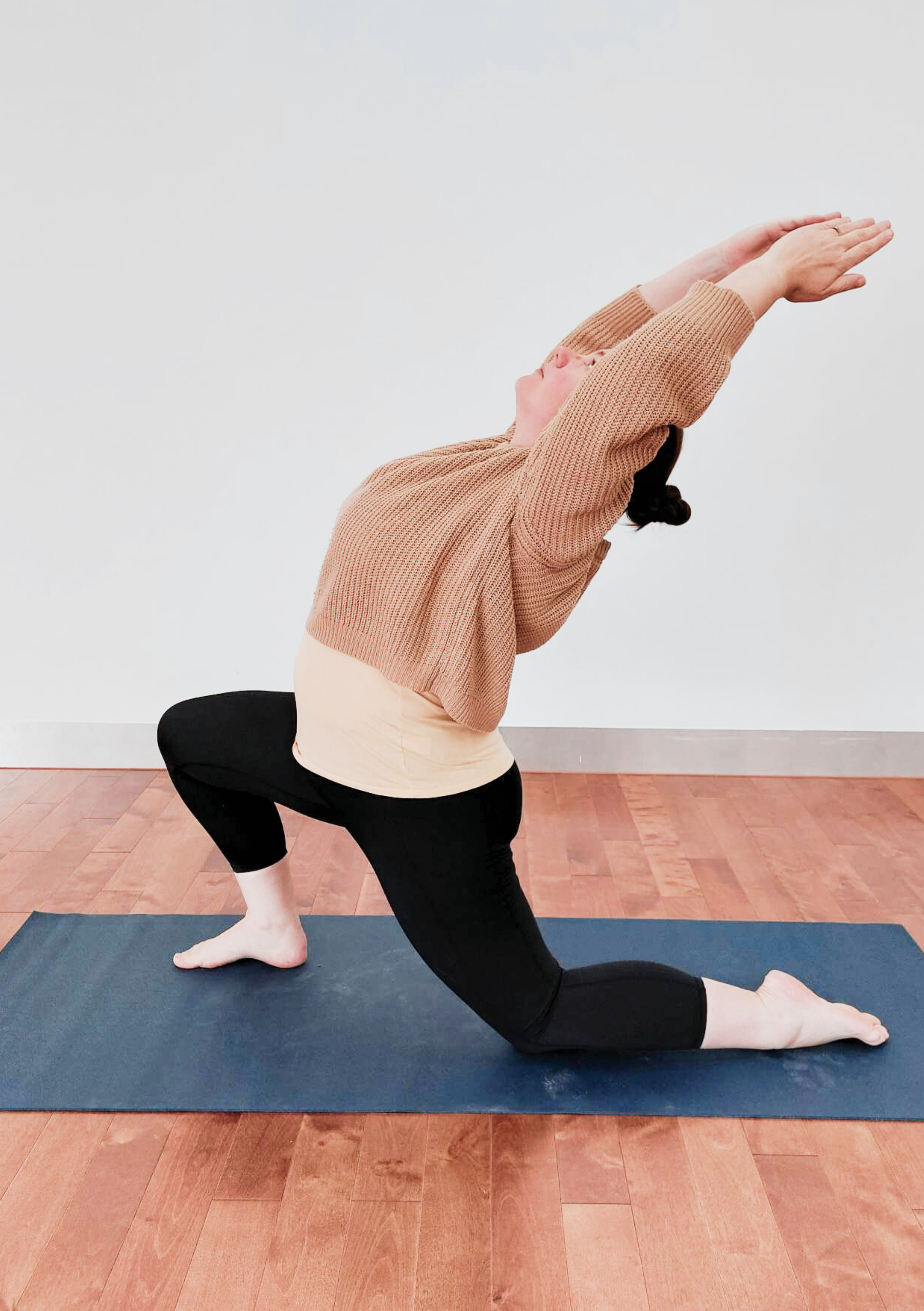 Woman on a yoga mat in a low lunge position with right leg forward and looking upwards with arms above the head